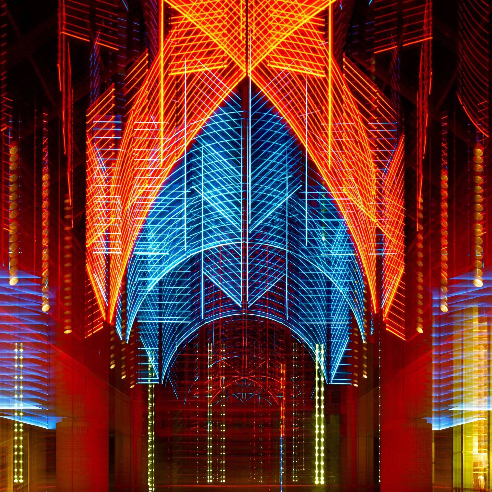 Colorful light patterns forming abstract geometric shapes with a mix of red, blue, and yellow neon lines in an arch-like arrangement.