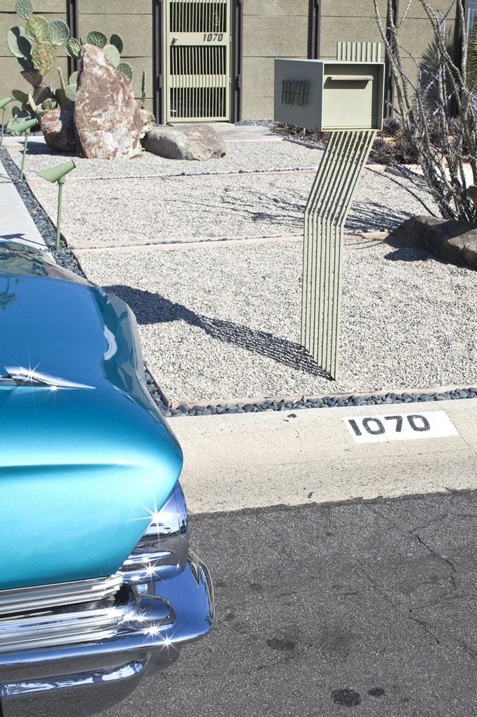 Front yard with modern mailbox, dry landscaping with rocks and cacti, turquoise vintage car, and house number 1070 on curb and gate.