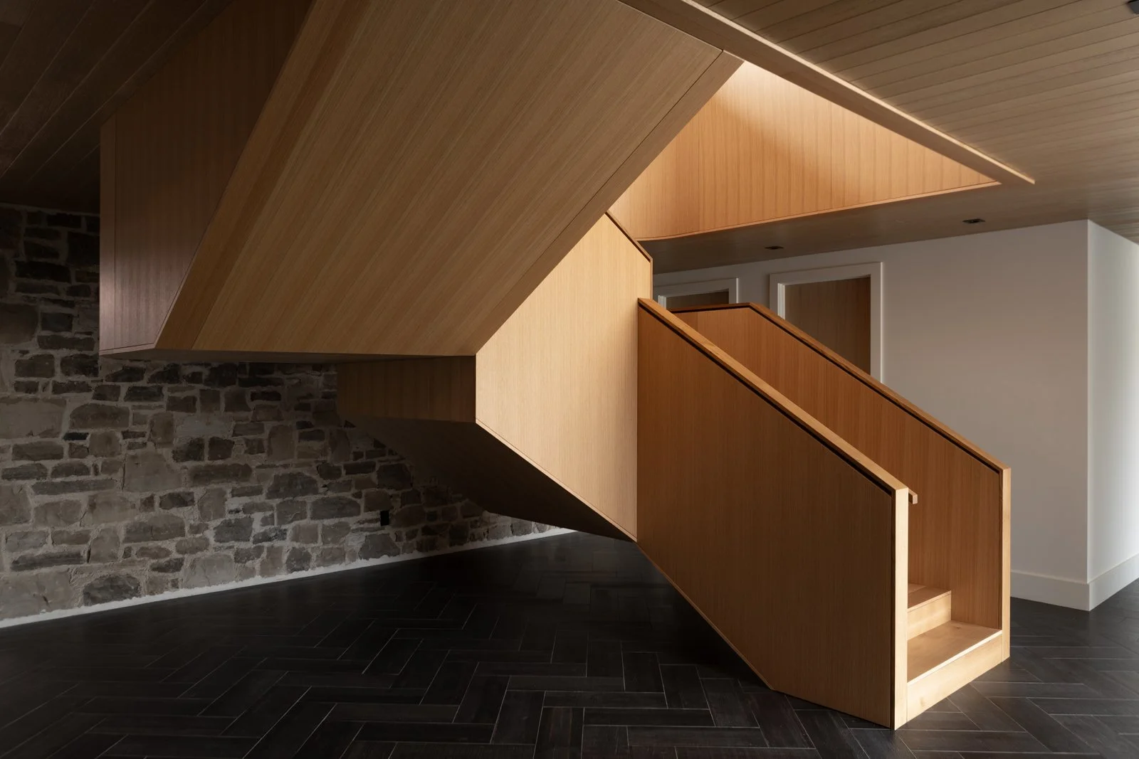 A striking modern staircase featuring warm wood paneling and clean geometric lines, designed for a luxury custom-built home in Ontario by Carter Allen.