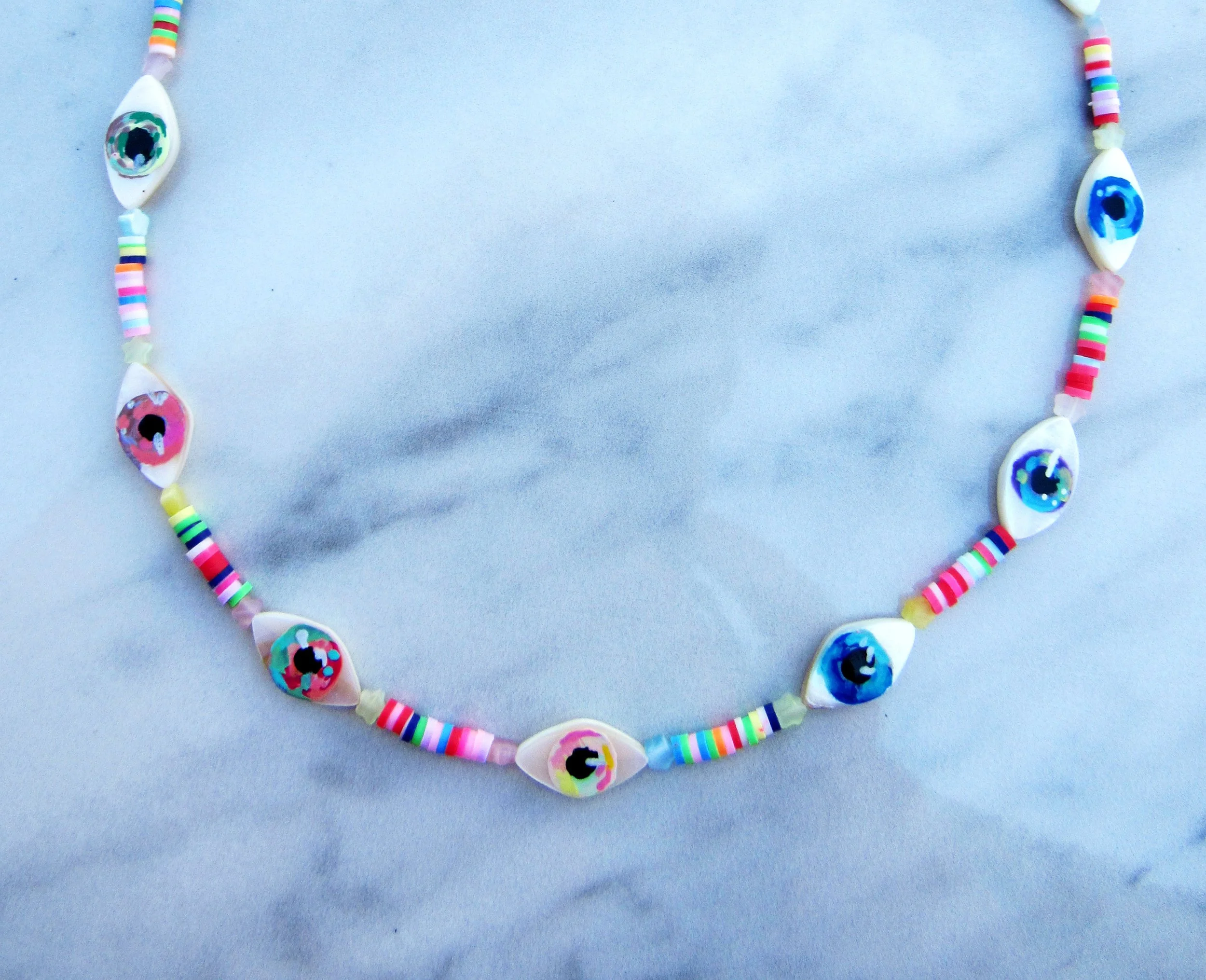 a colorful necklace made out of multicolored beads divided into sections by hand painted clay eyeballs of various colors