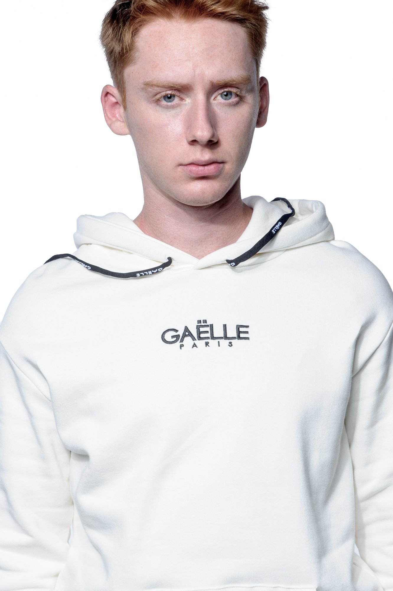 Person wearing a white Gaelle Paris hoodie with a serious expression.