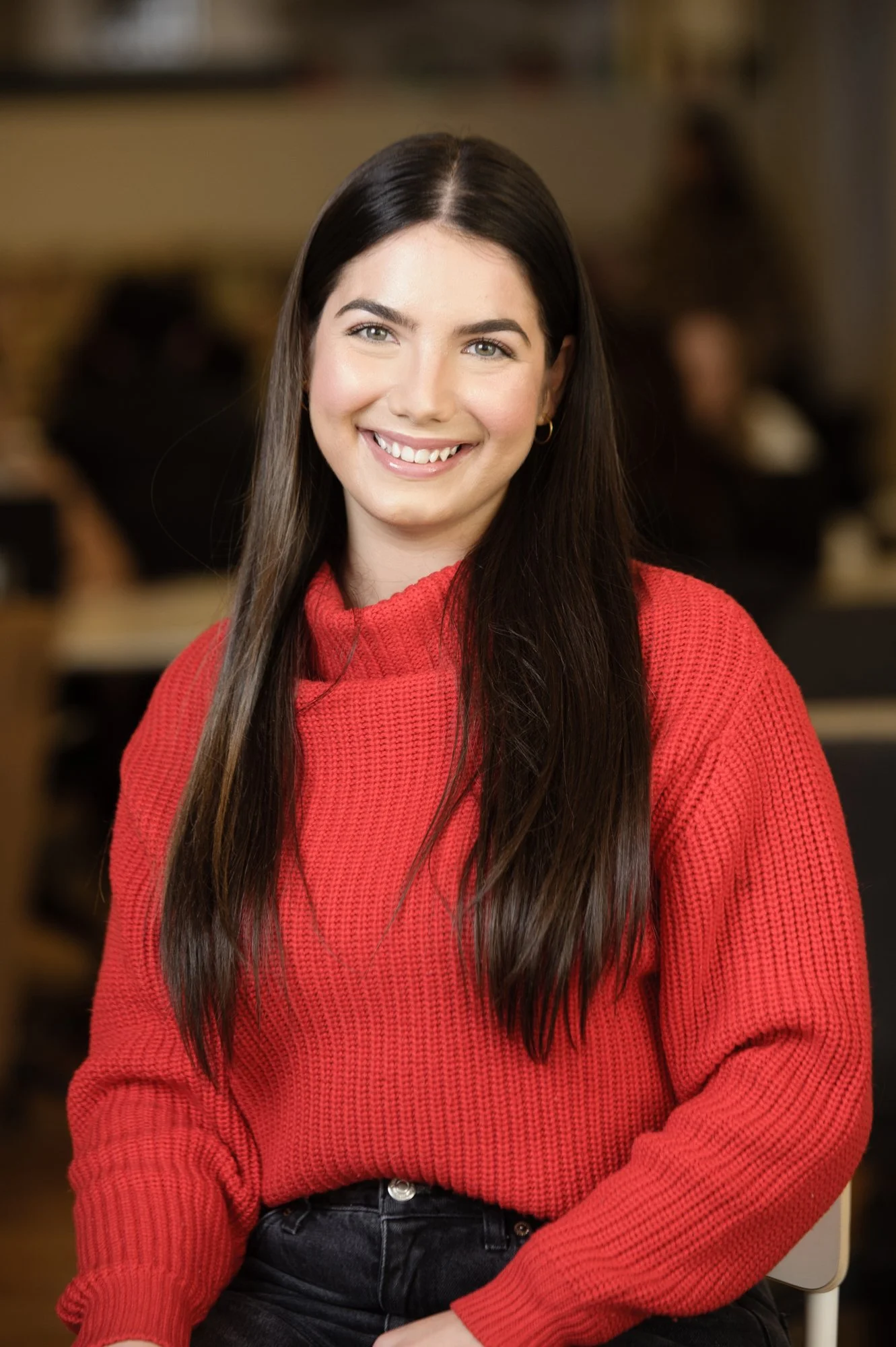 Smiling person wearing a red sweater sitting indoors