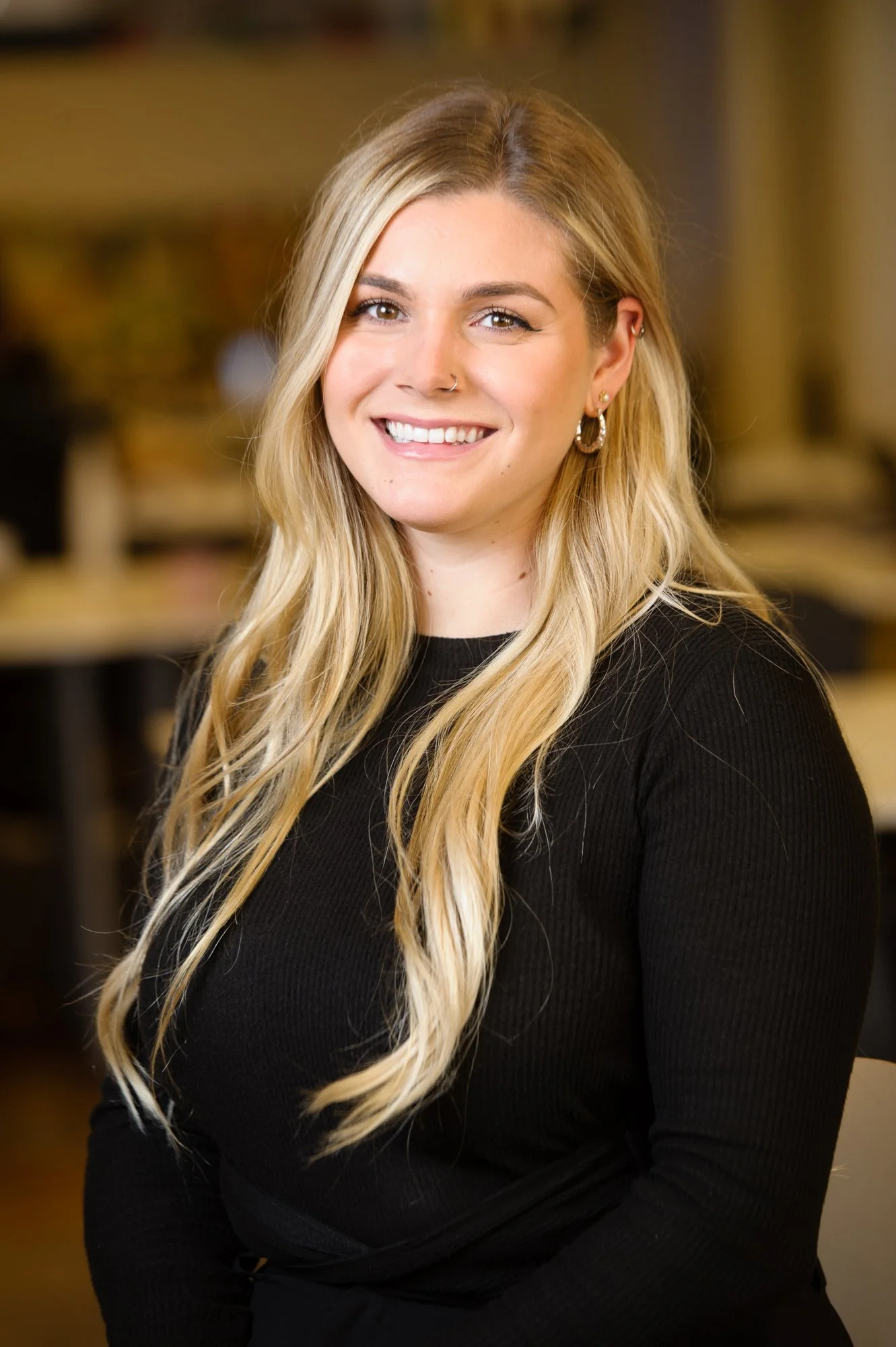 Smiling woman with long blonde hair wearing a black sweater indoors.