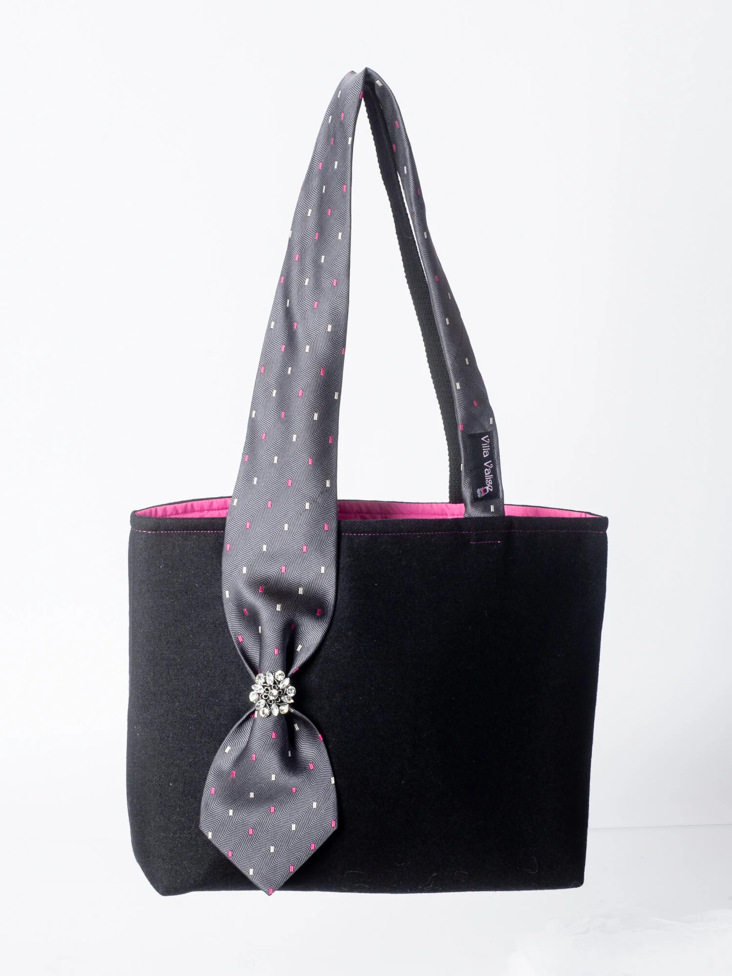 Black handbag with a gray dotted tie handle and decorative brooch, pink interior, and minimalist design.