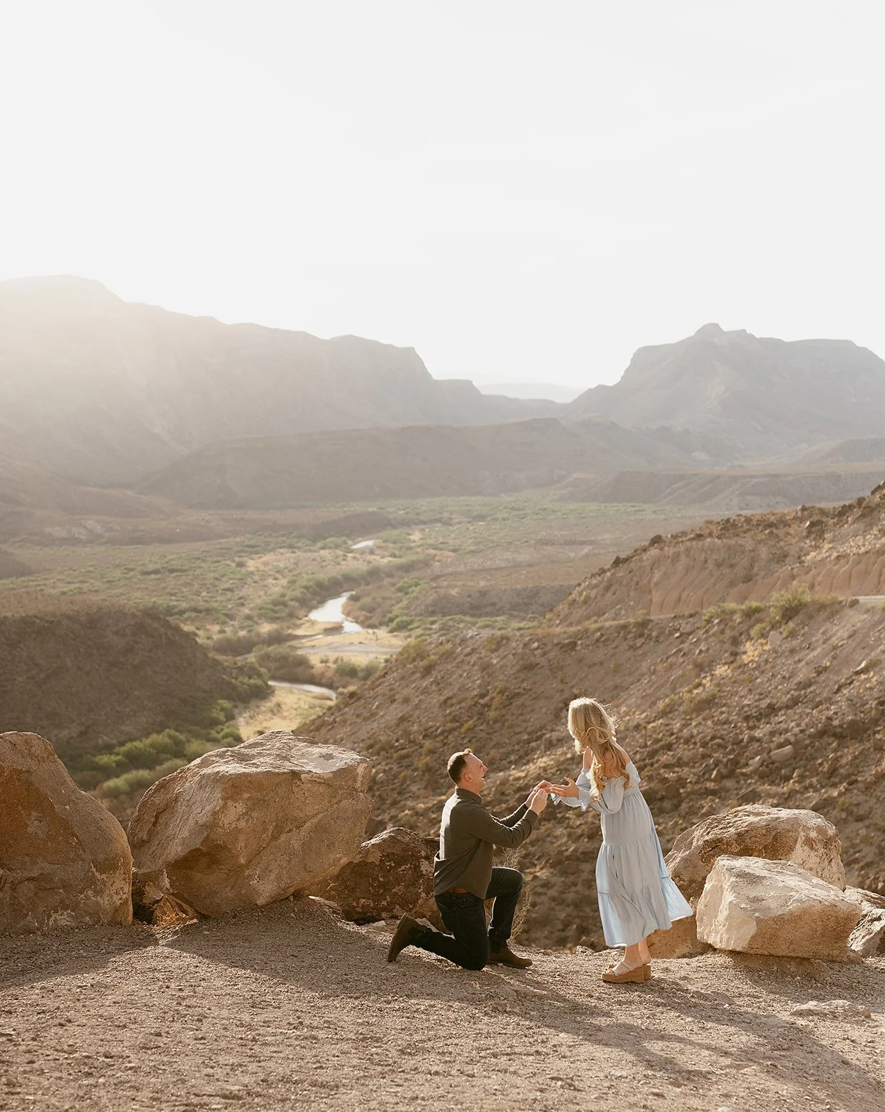 A man proposing marriage to a woman in a mountainous desert landscape during sunset.