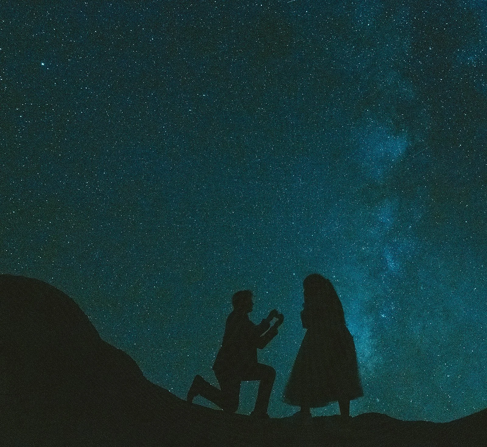 Silhouettes of a man proposing to a woman under a starry night sky