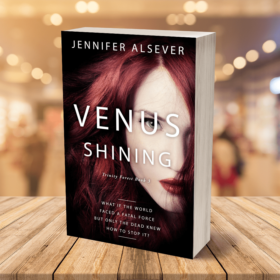 A paperback book titled 'Venus Shining' by Jennifer Alsever, featuring a cover image of a woman with long red hair and striking makeup, displayed on a wooden table with a blurred store background.
