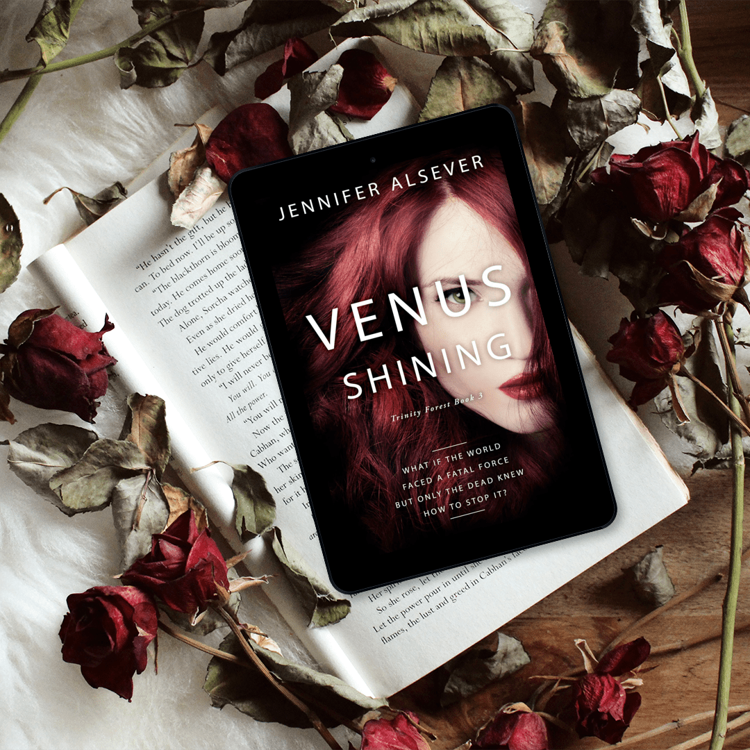 A digital tablet displaying the book cover of 'Venus Shining' by Jennifer Alsver, placed on an open book surrounded by dried roses and leaves on a wooden surface.