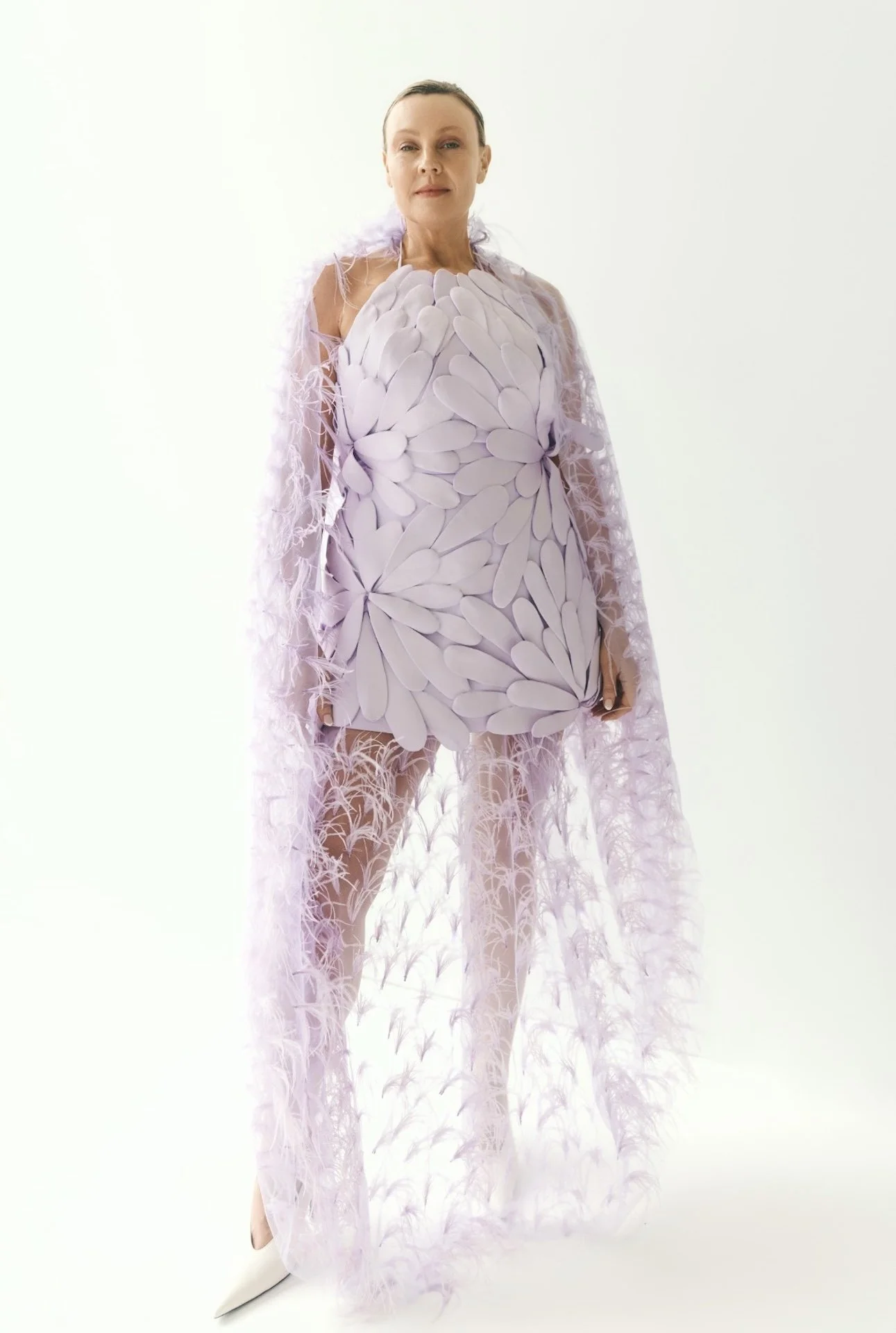 Model wearing an avant-garde lavender dress with layered petal details and a feathered sheer train