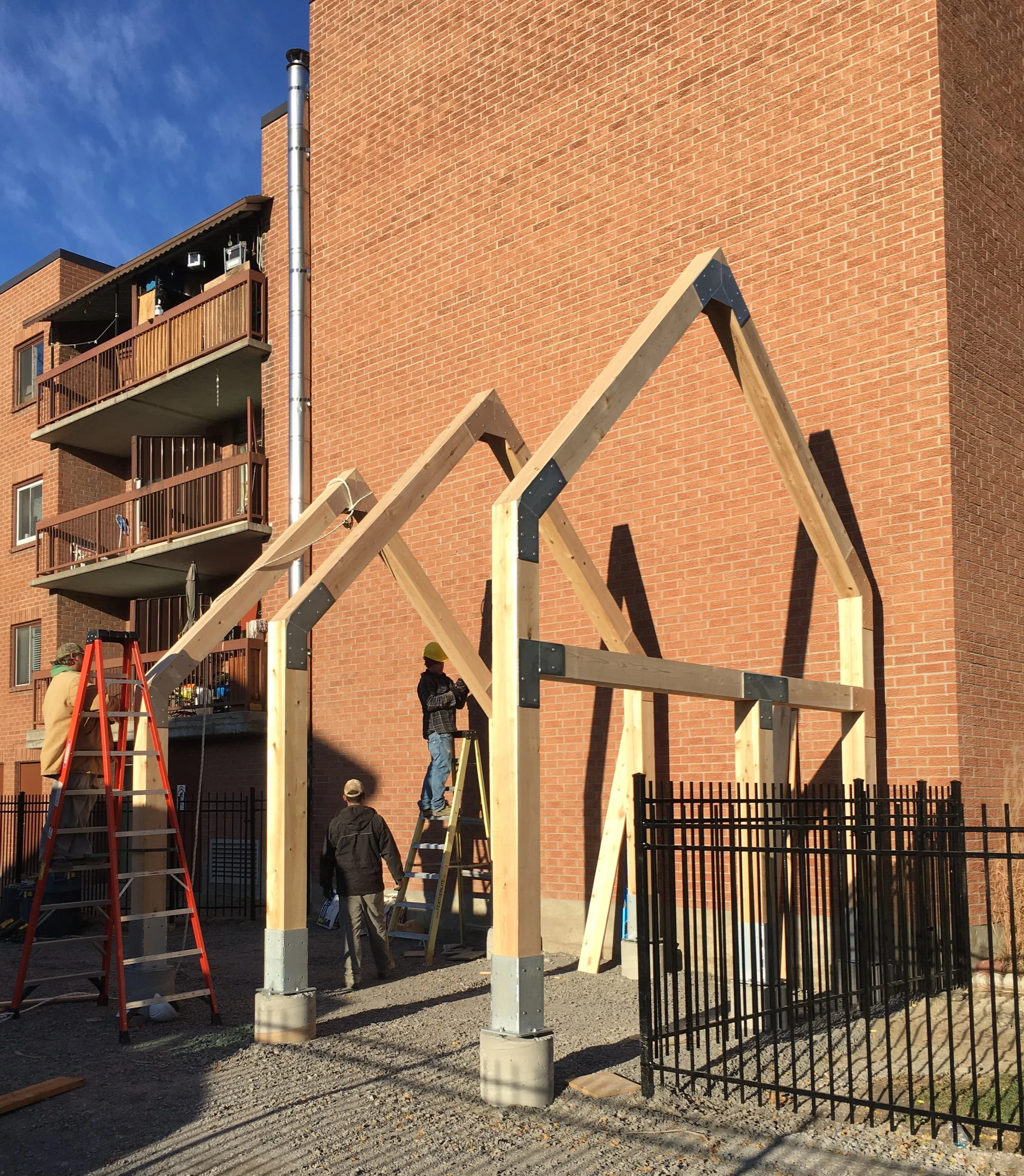 Custom Cedar Structure,  building a wooden structure with a brick building in the background.