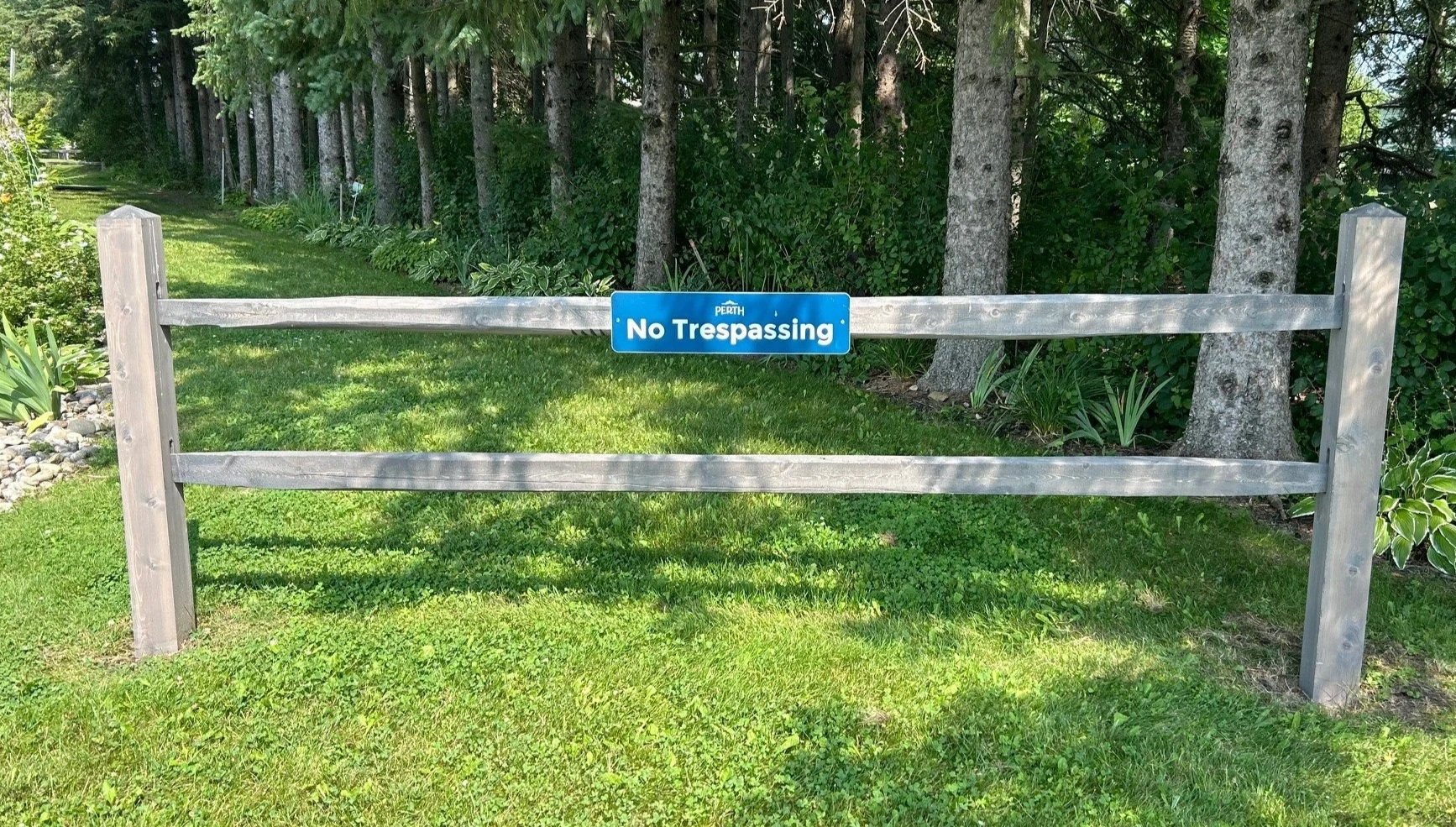 Urban Cedar Post and Rail fence pre-stained Grey-'No Trespassing' in front of a grassy area and trees.