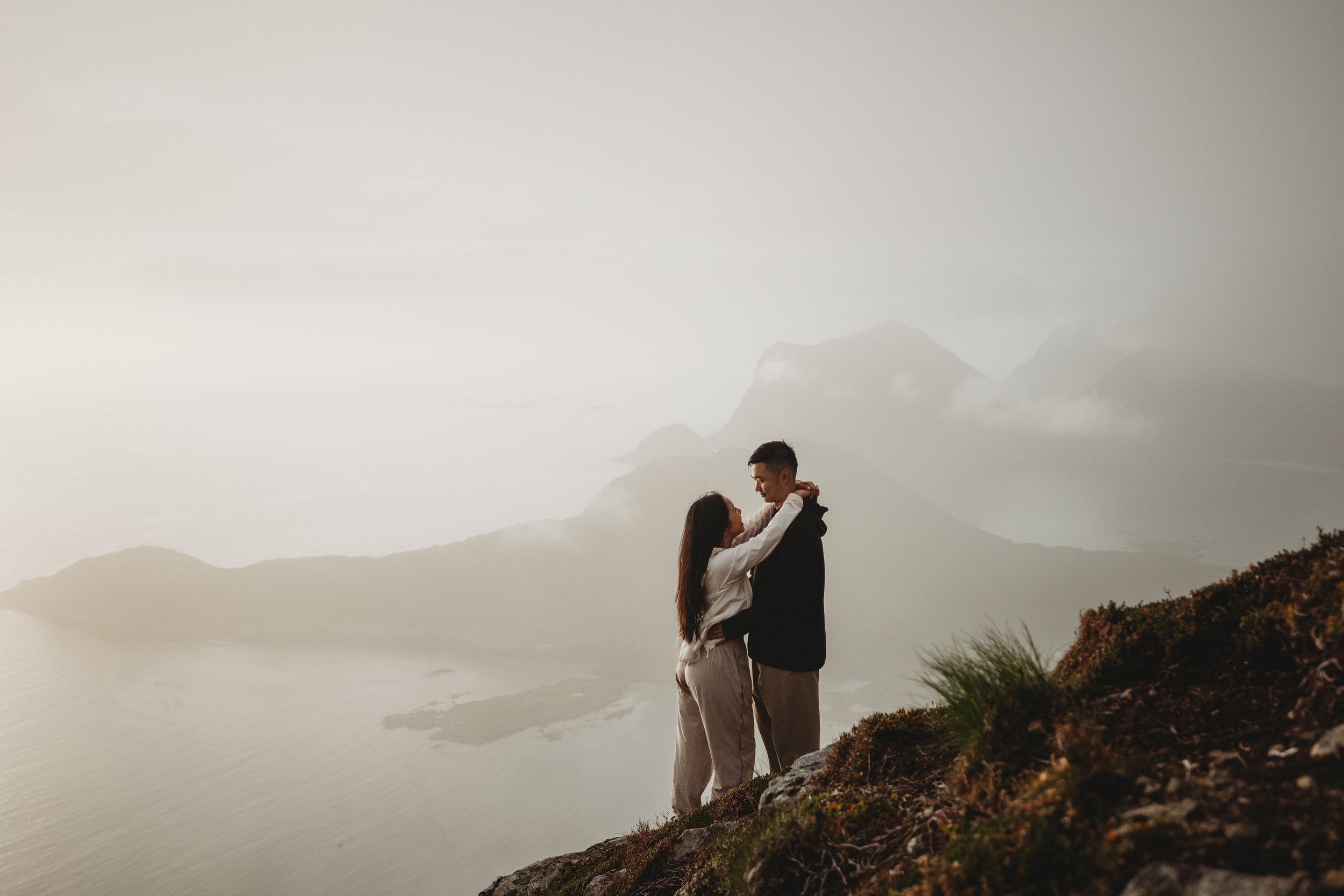 A couple standing on Offersøykammen mountain edge, embracing with a misty mountain landscape in the background.