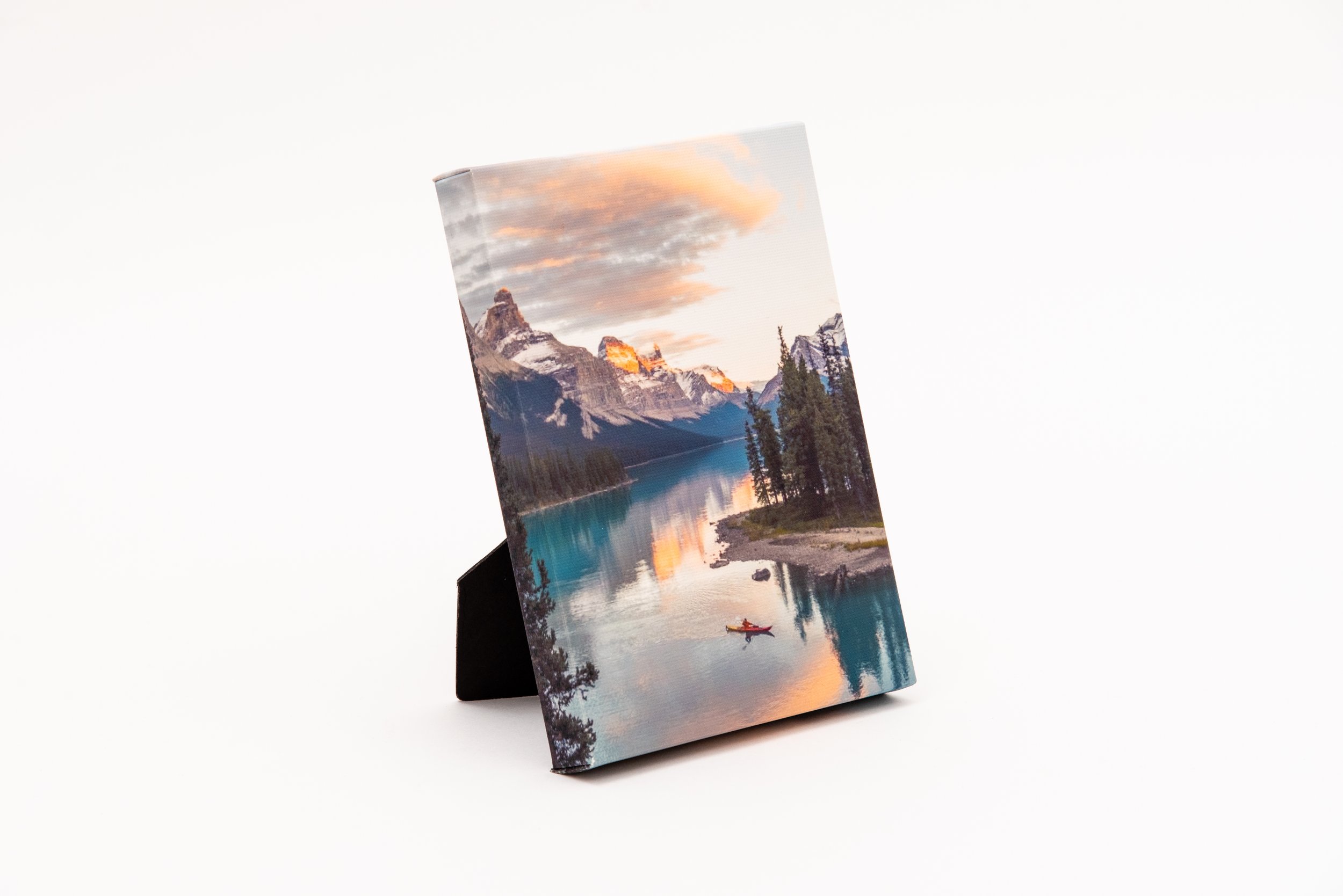 Canvas photo of a small tabletop stand with a scenic landscape image of mountains, a lake, and a person kayaking.
