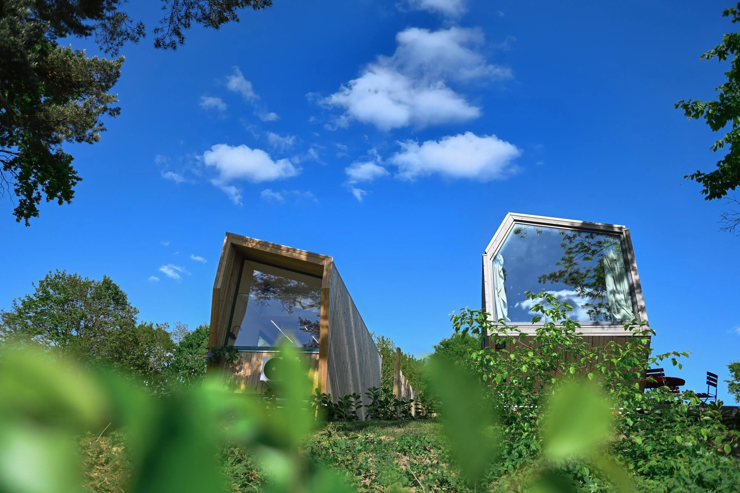 Zwei Tiny Houses am Salemer See mit Panoramafenster in einer grünen, bewaldeten Umgebung bei blauem Himmel mit Wolken.