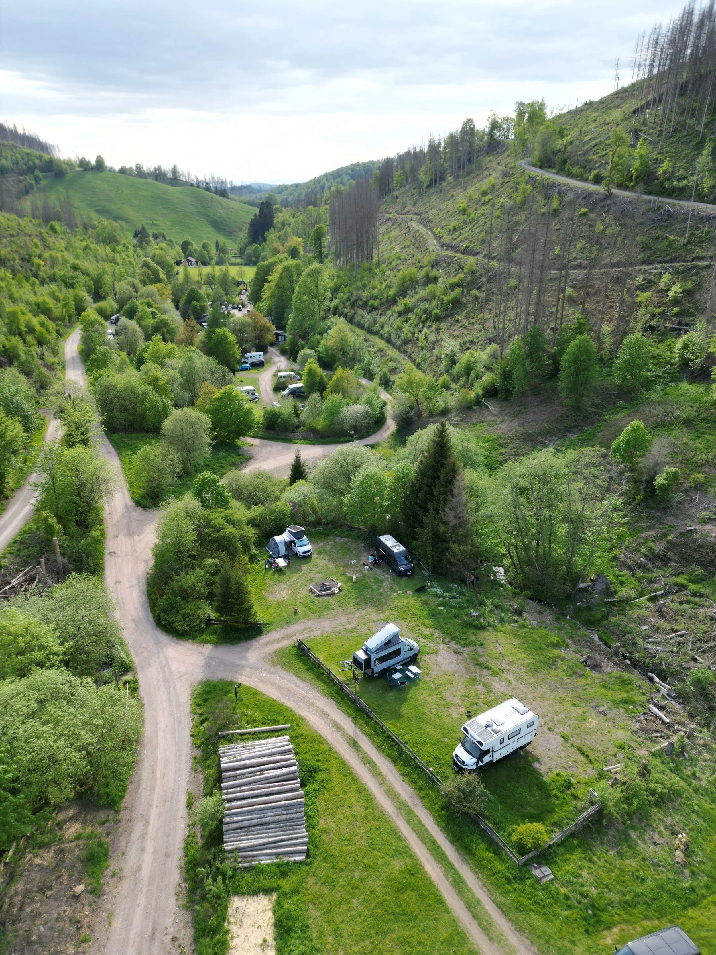 Campingplatz Harz Hideaway in einem grünen Tal mit Wohnmobilen, Zelten und Waldgebiet, umgeben von Hügeln und Bäumen.