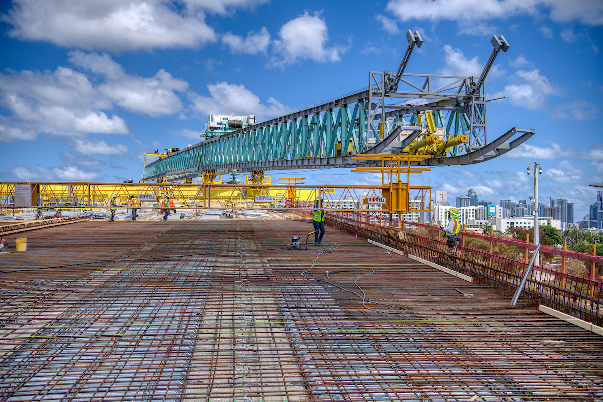 Construction workers on a building site with a large crane structure against a city skyline and partly cloudy sky.