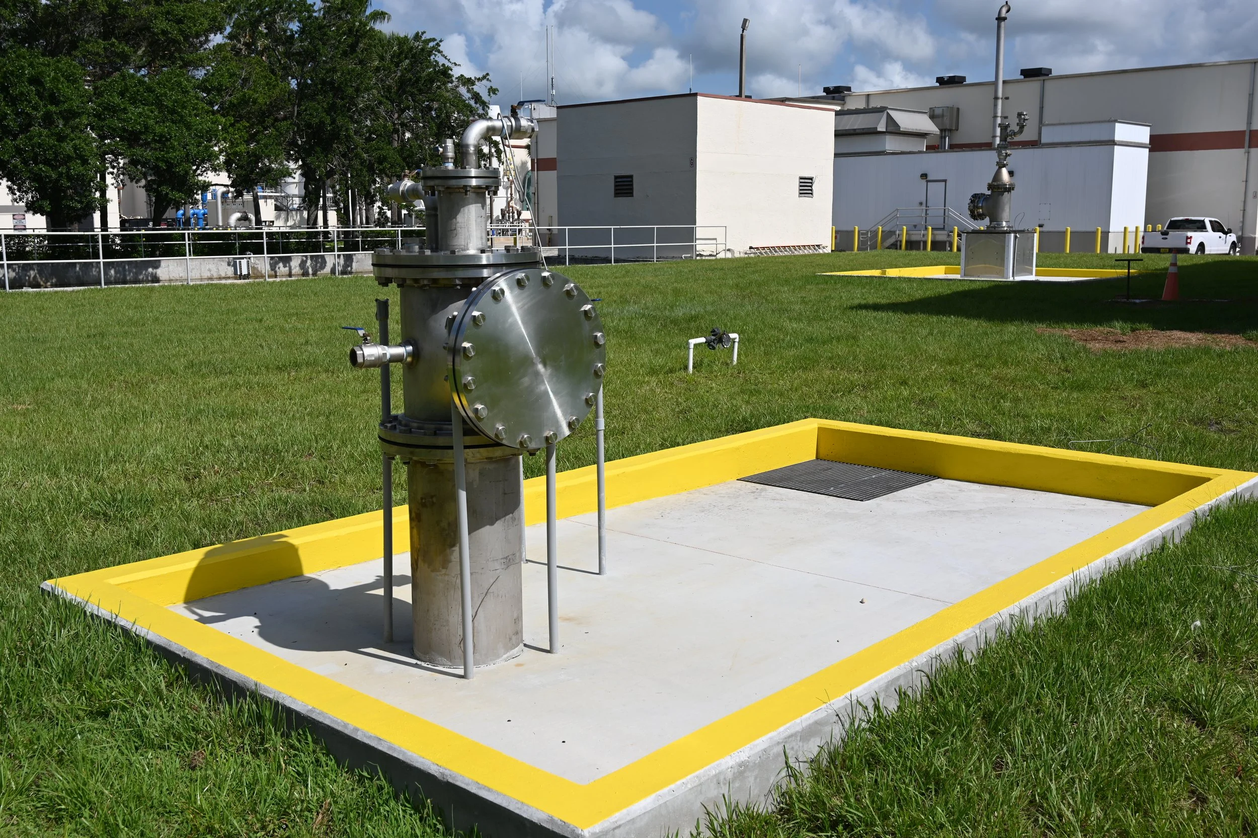Industrial equipment and piping outside a building, with a grassy area and cloudy sky.