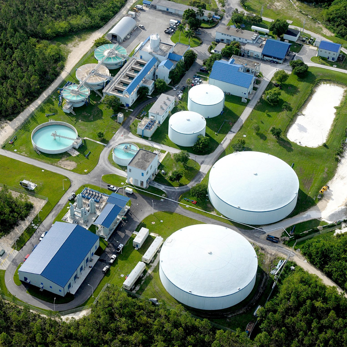 Aerial view of a water treatment plant with large circular tanks, processing buildings, and surrounding greenery.