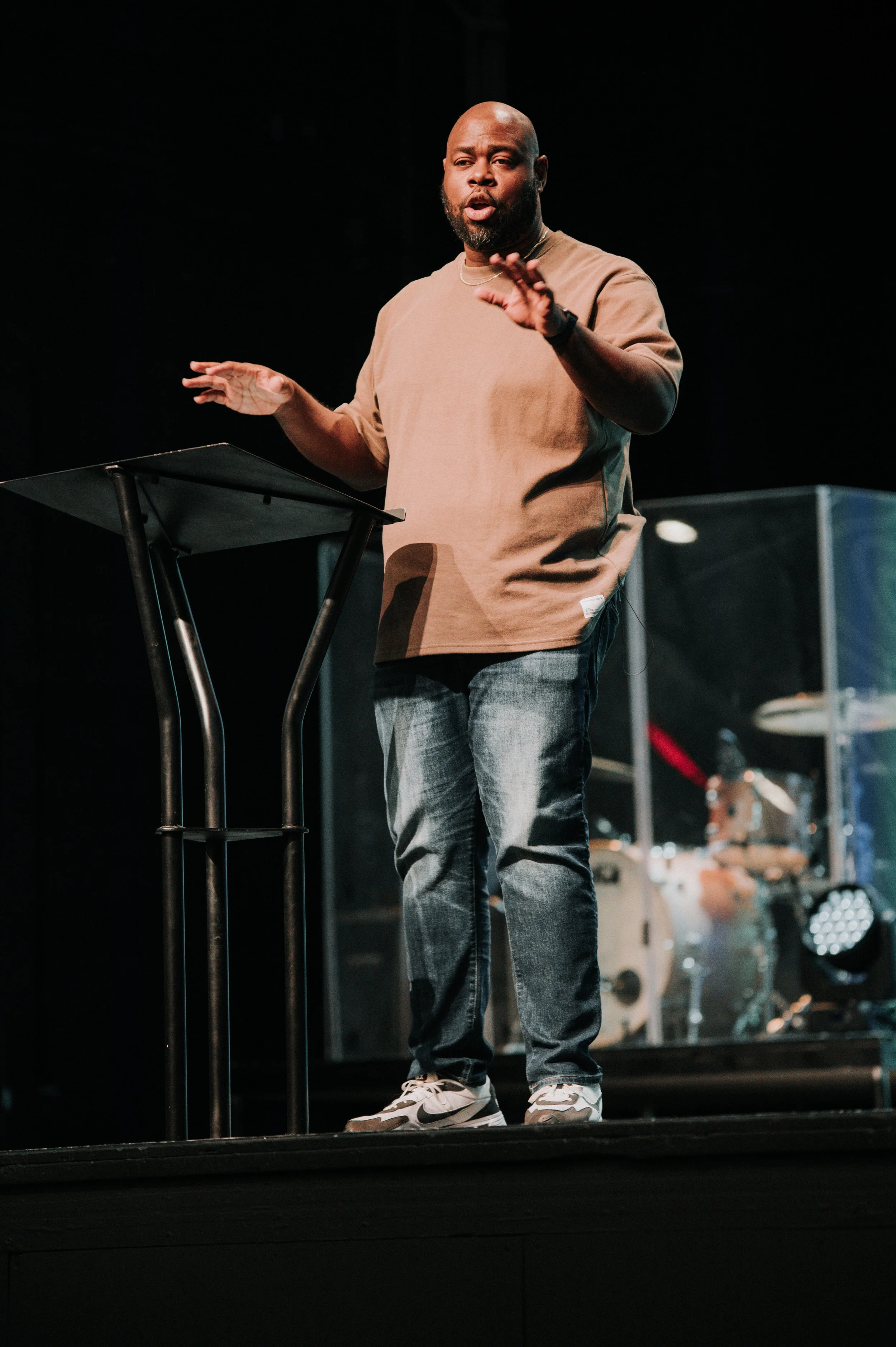 Charlie Mitchell speaking at a podium on stage with a band in the background.