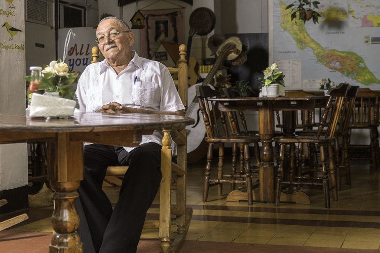 Restaurant owner seated at a wooden table inside his Curaçao restaurant
