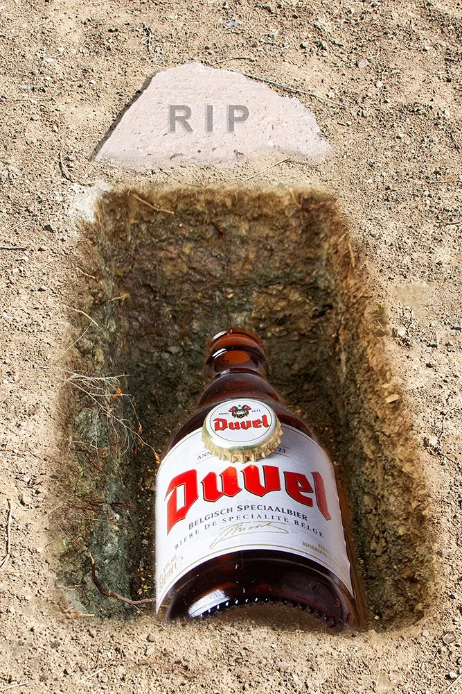 Duvel beer bottle laid in an open grave beneath an RIP headstone, conceptual still life photography
