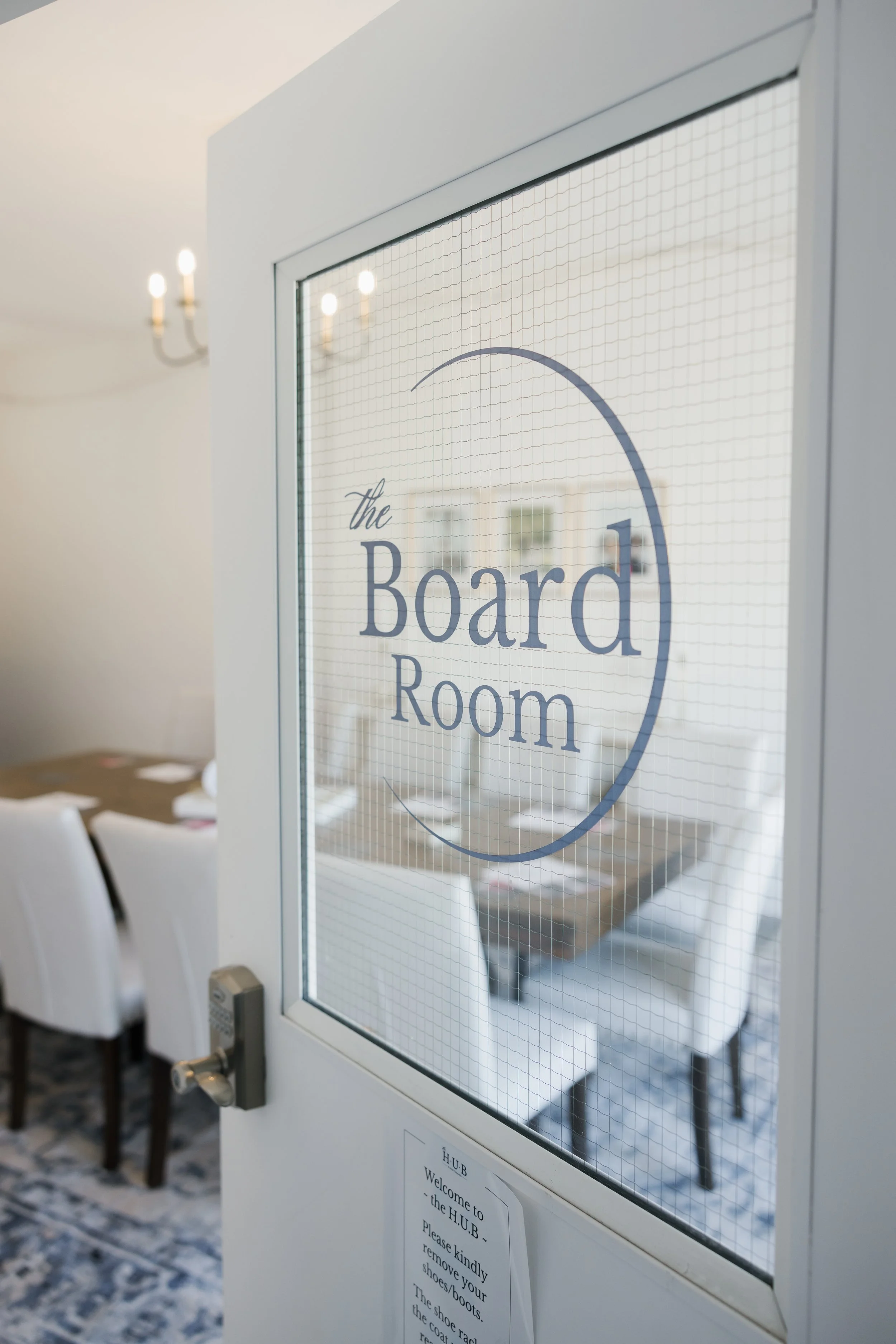 A door with a sign that reads 'the Board Room' in a conference room, with chairs and tables visible outside.