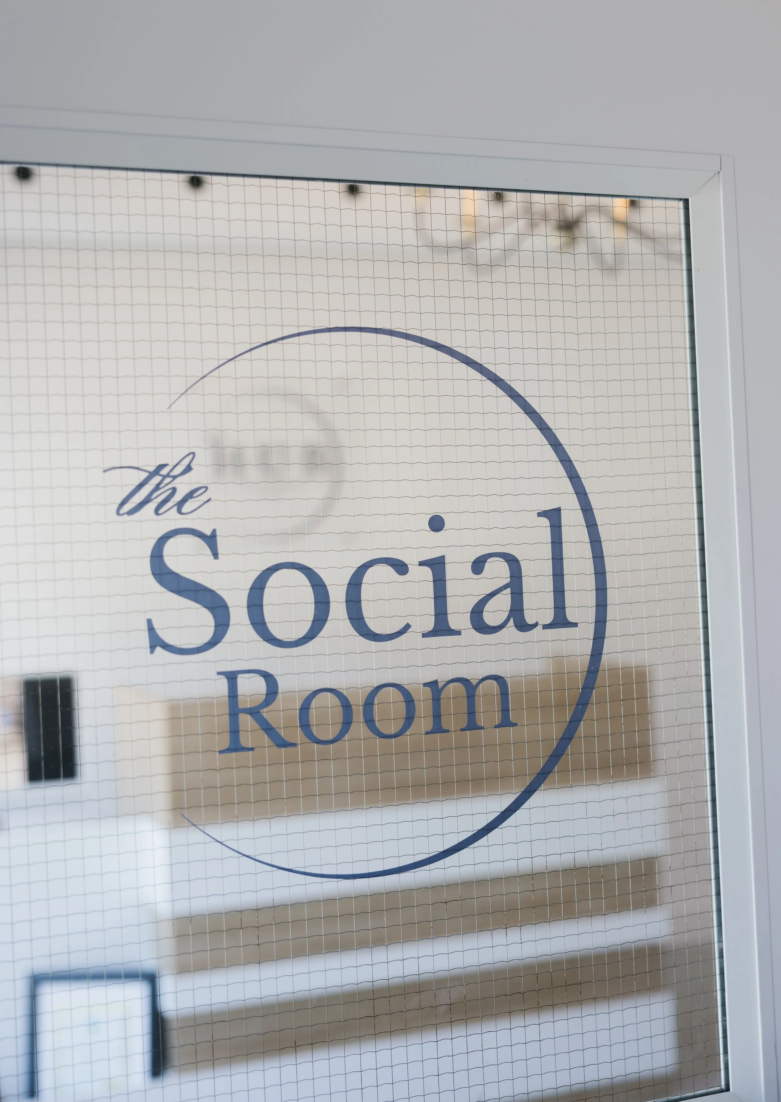 Door with a sign reading 'The HUB Social Room,' and a view of a conference room inside with shelves, a table, and a chandelier.