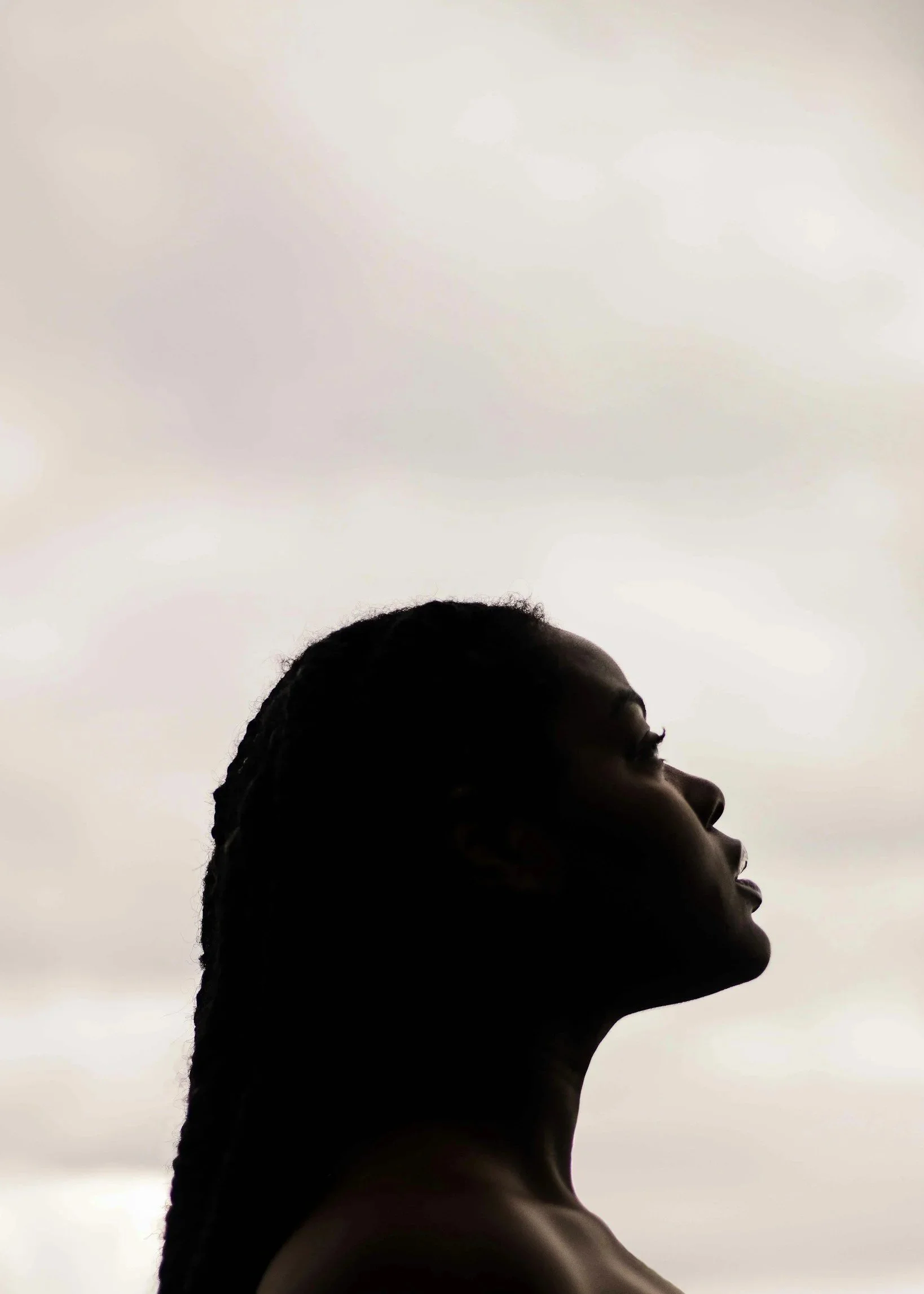 Silhouette of a woman with braided hair looking up at a cloudy sky.