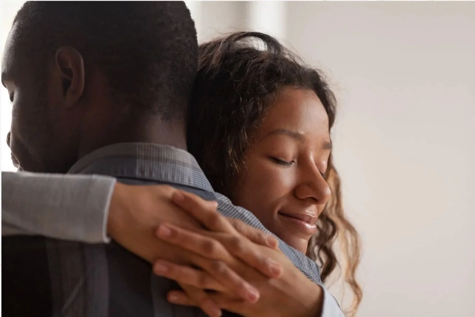 A man and a woman hugging, with the woman smiling with her eyes closed.