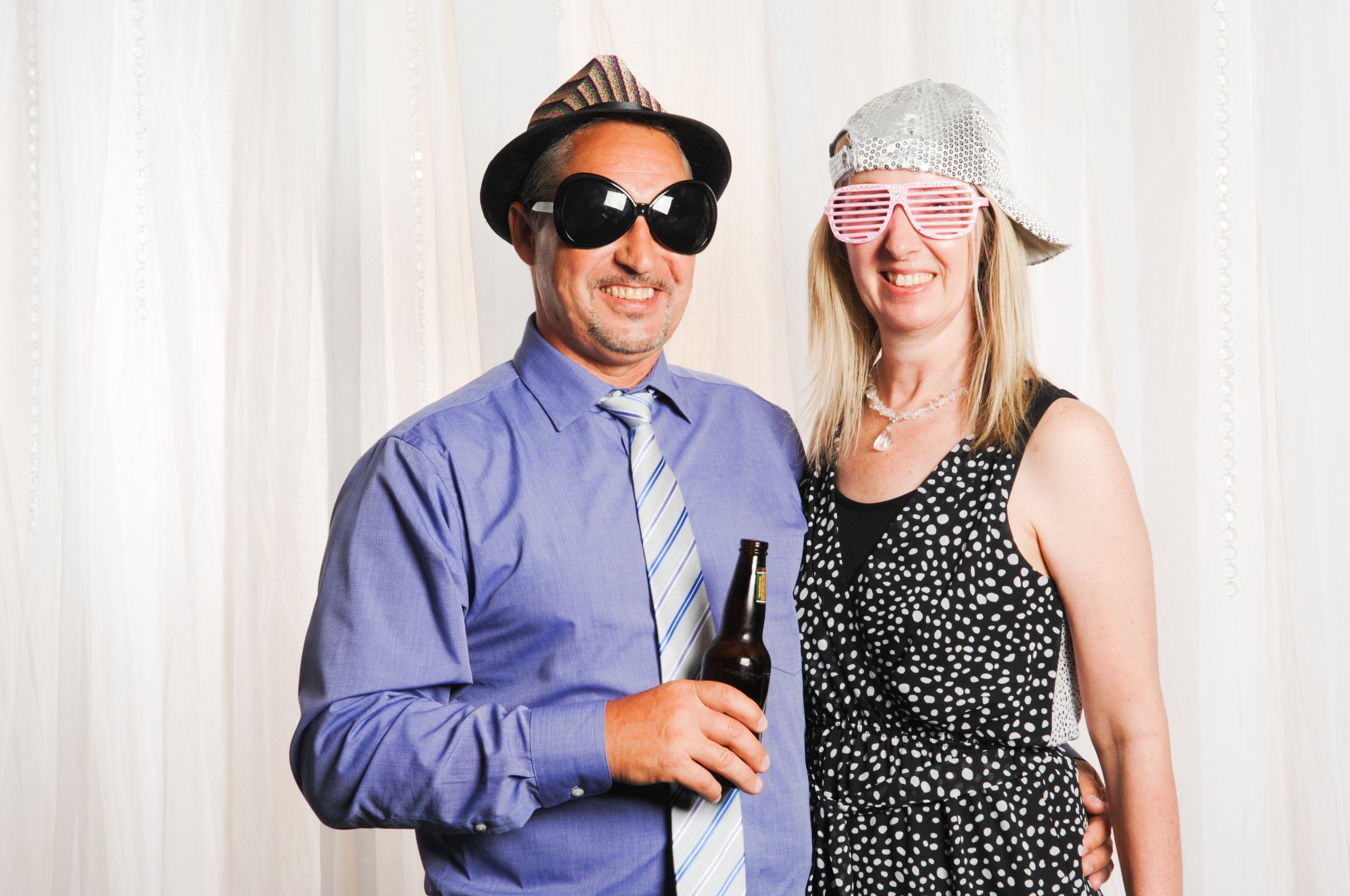 Man and woman wearing funny hats and sunglasses; the man holds a beer bottle.