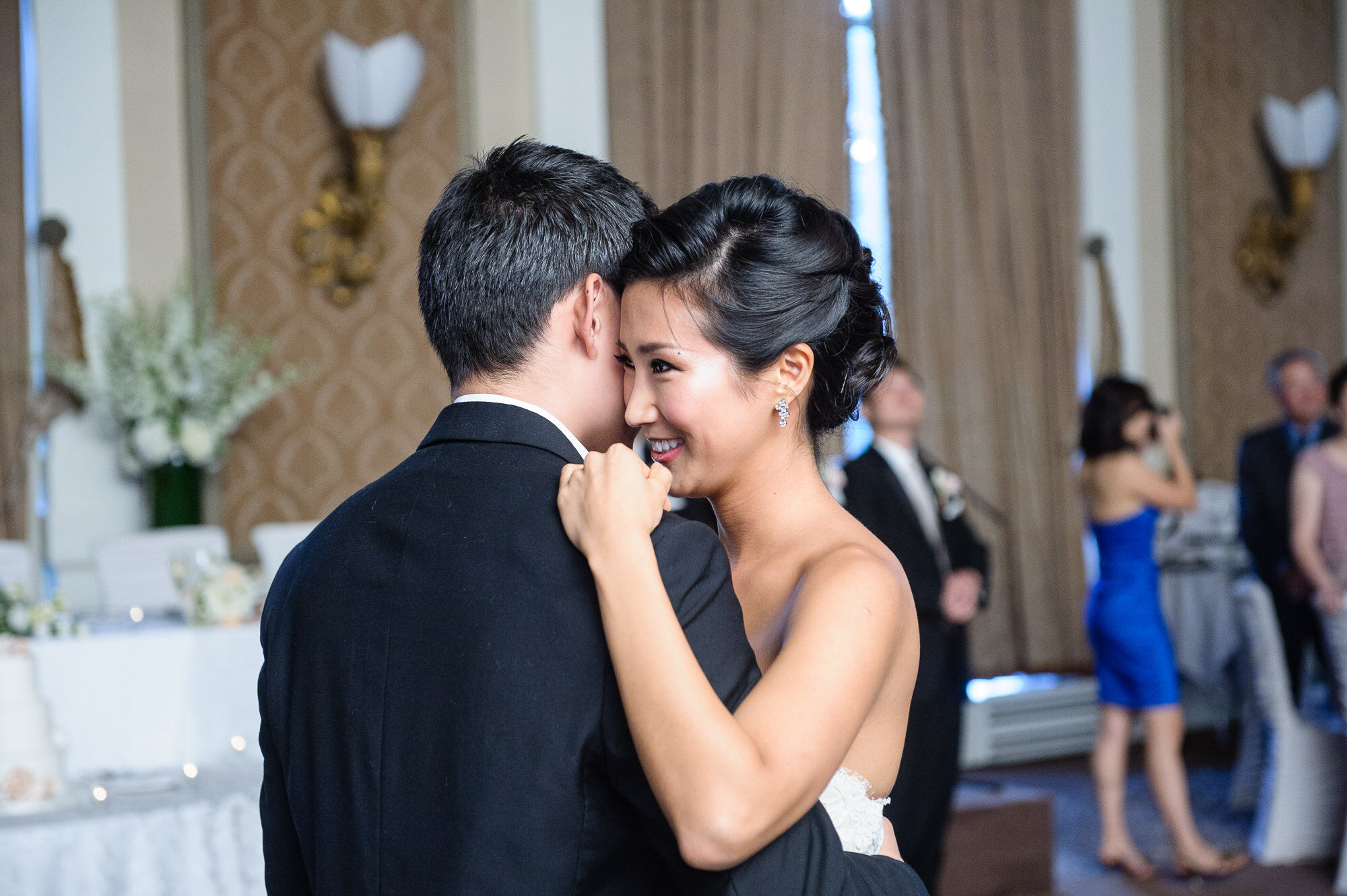 A bride and groom dancing closely at a wedding reception, surrounded by guests in a decorated room.