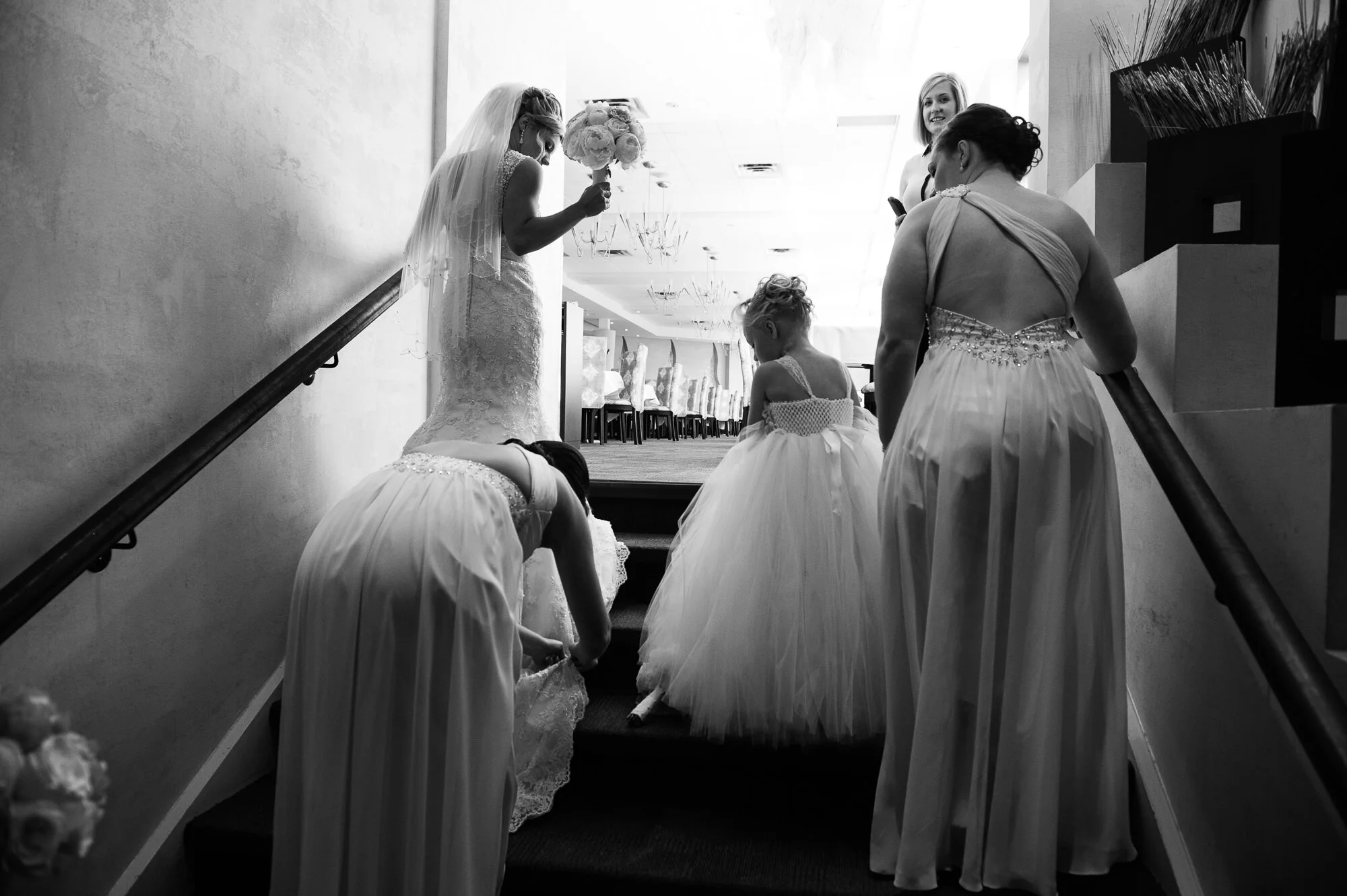 Bride and bridal party on stairs, child in flower girl dress, black and white.