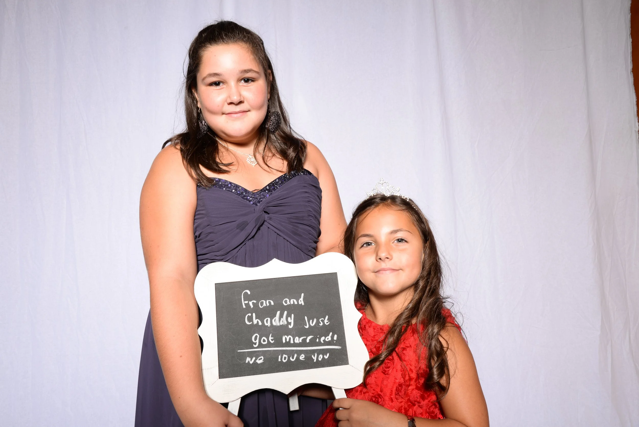 Two girls in formal dresses holding a chalkboard sign at a wedding.