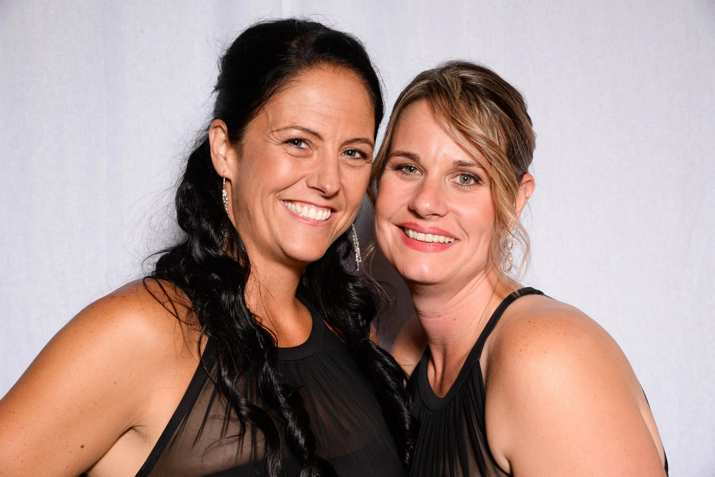 Two women smiling in black dresses against a light background