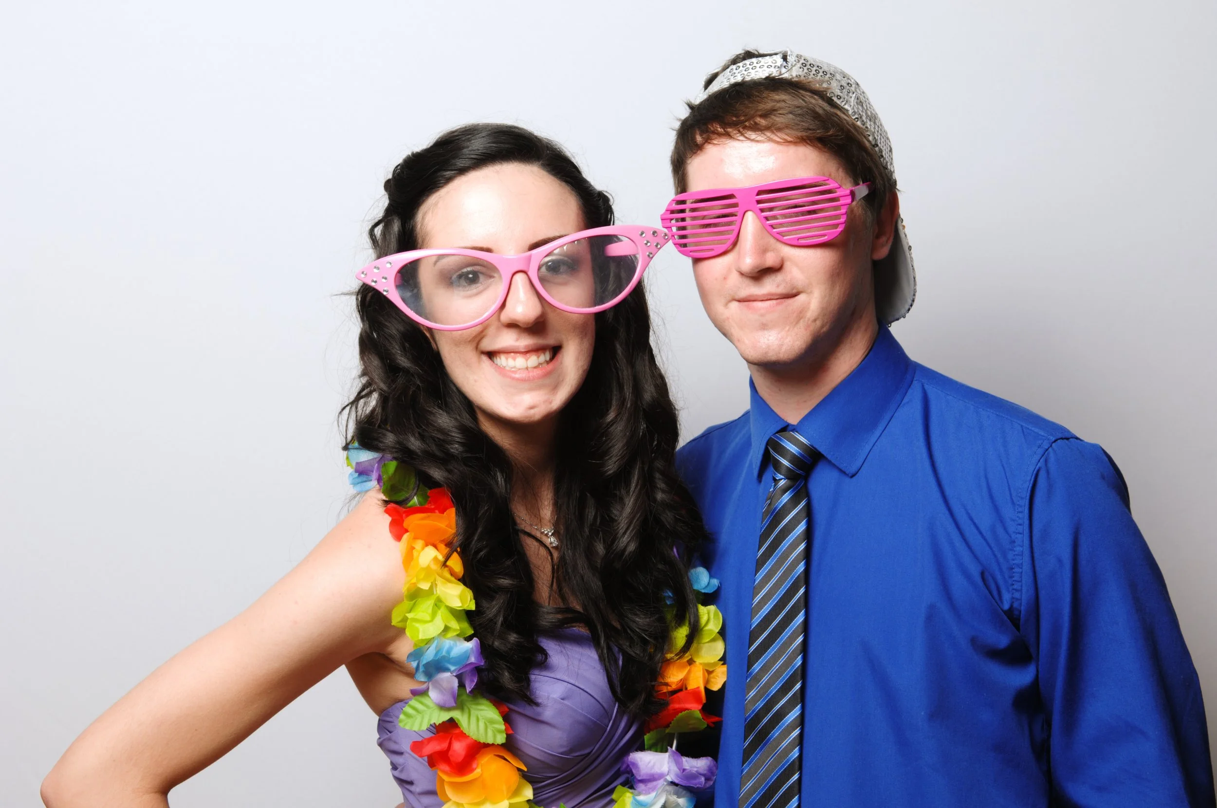 Two people wearing novelty glasses and colorful accessories, smiling in a photo booth setting.