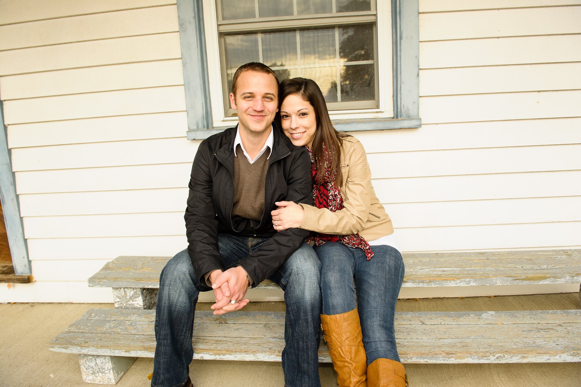 Couple sitting on porch steps hugging, wearing casual clothing, in front of white wooden siding.