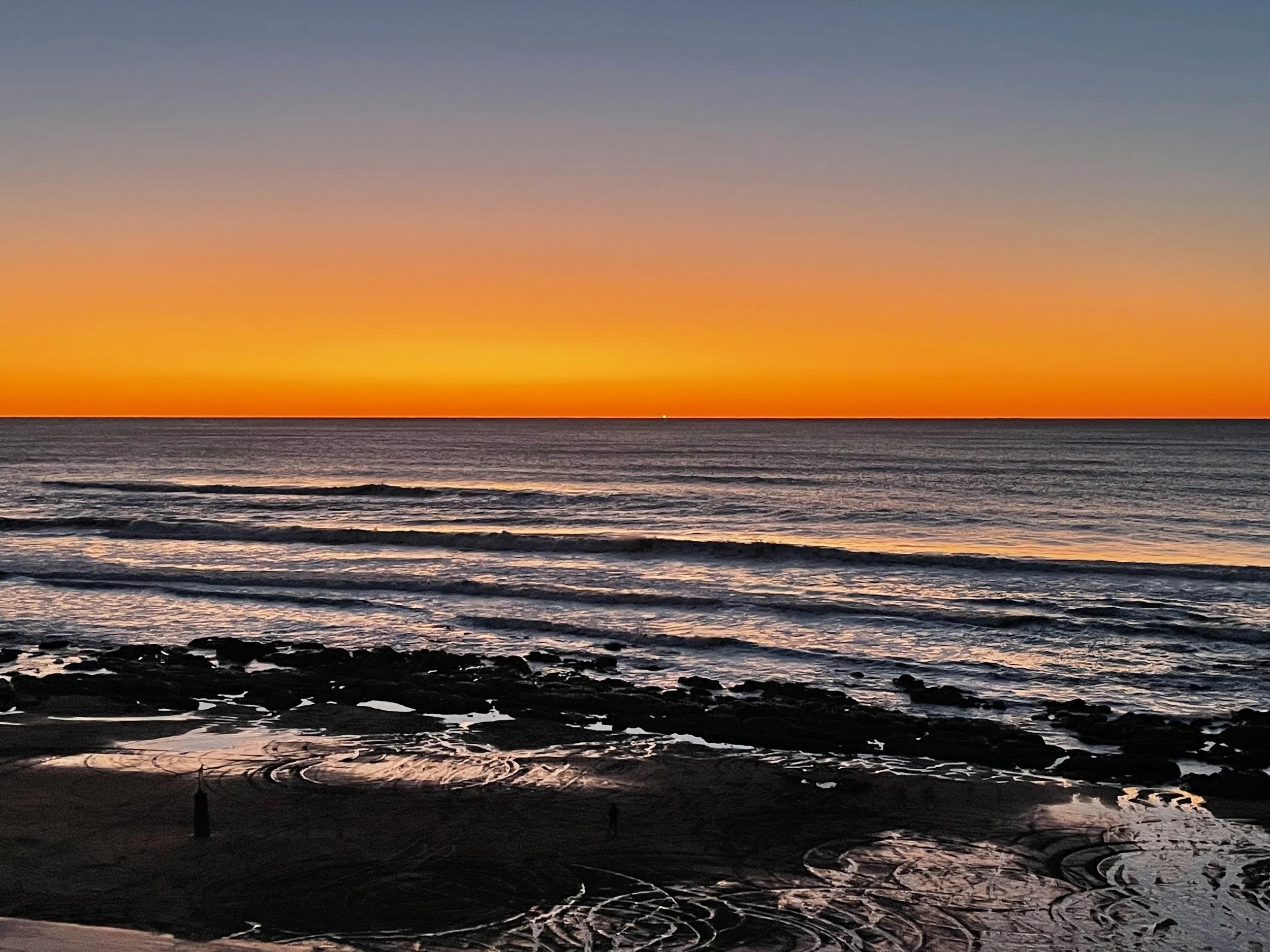 Sunset over the ocean with gentle waves and rocks on the beach