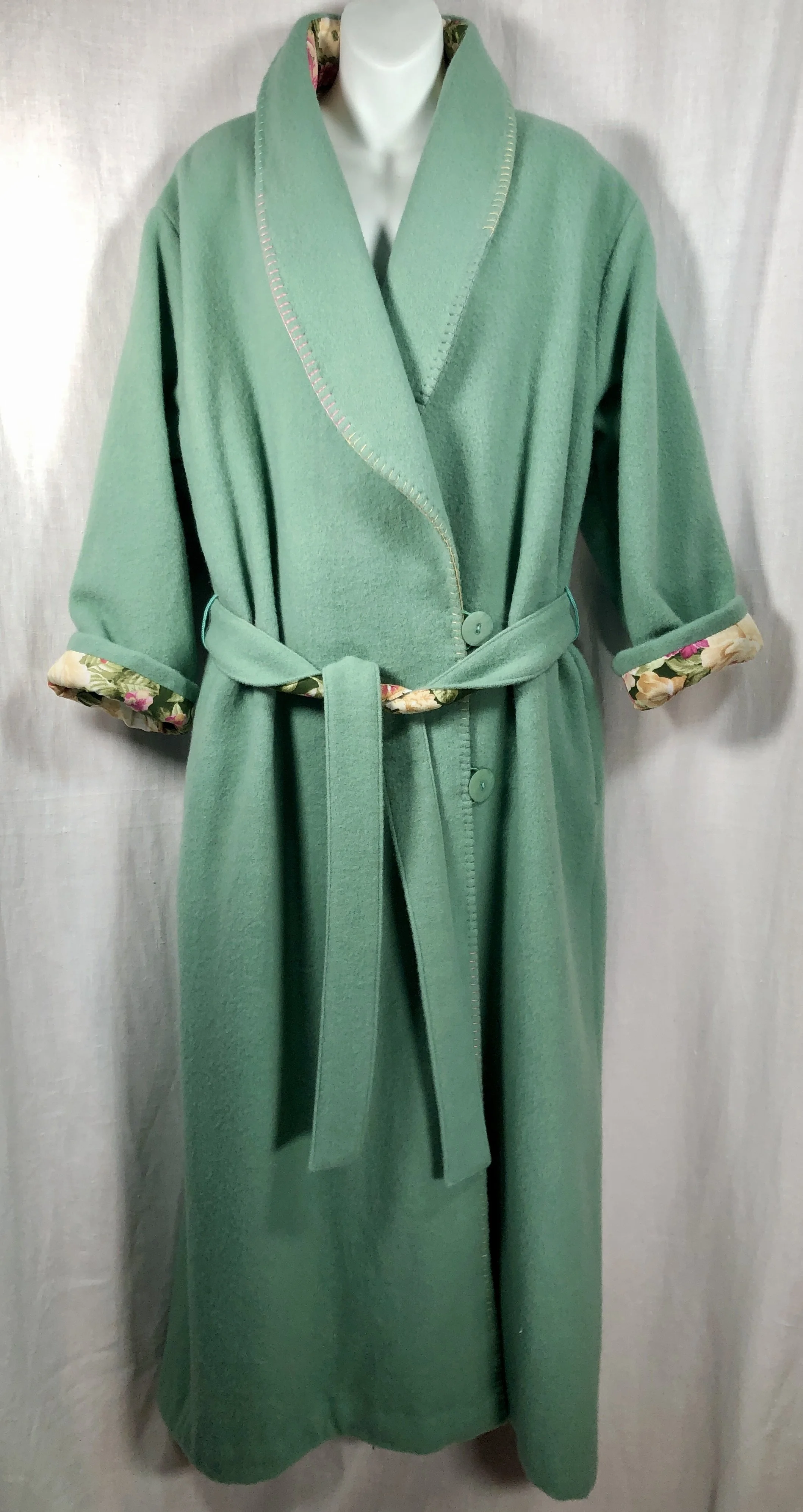A green wool coat with floral lining visible at the rolled-up cuffs and collar, displayed on a mannequin against a light-colored background.