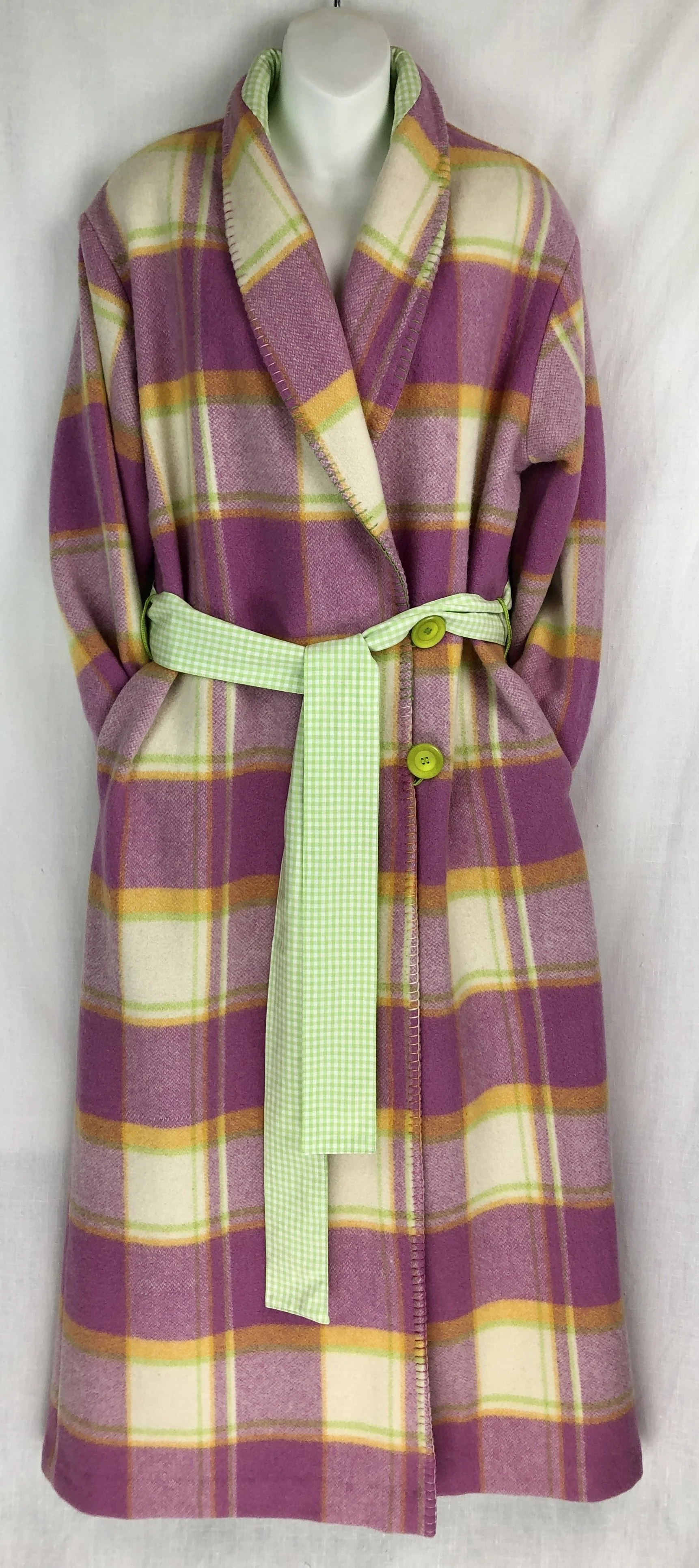 A long, plaid wool dressing gown in purple, yellow, and cream colors, with bright green buttons, a lime green checkered belt, and a green and white checkered collar lining, displayed on a mannequin against a white background.