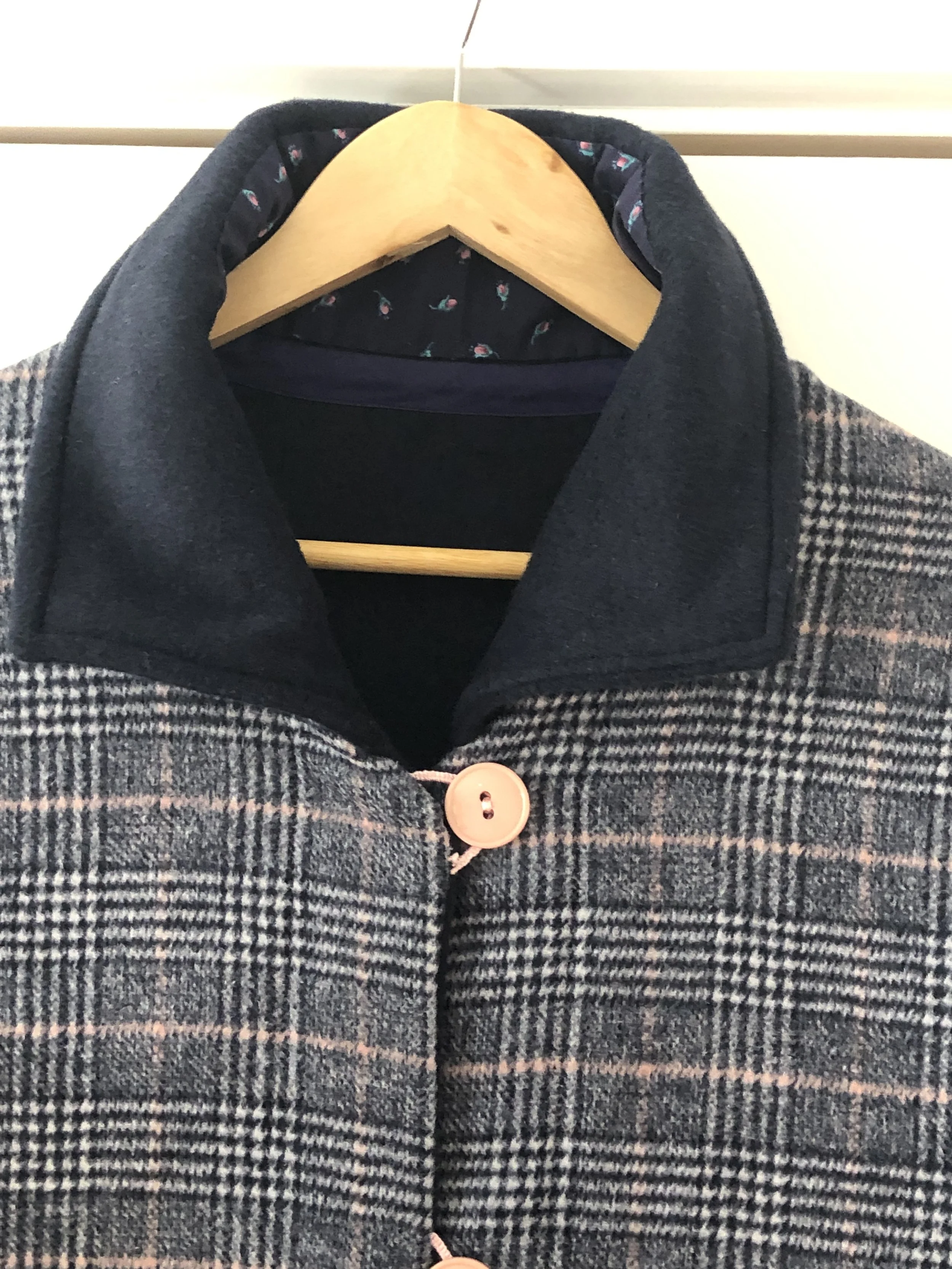 Close-up of a plaid dressing robe with pink buttons hanging on a wooden hanger.