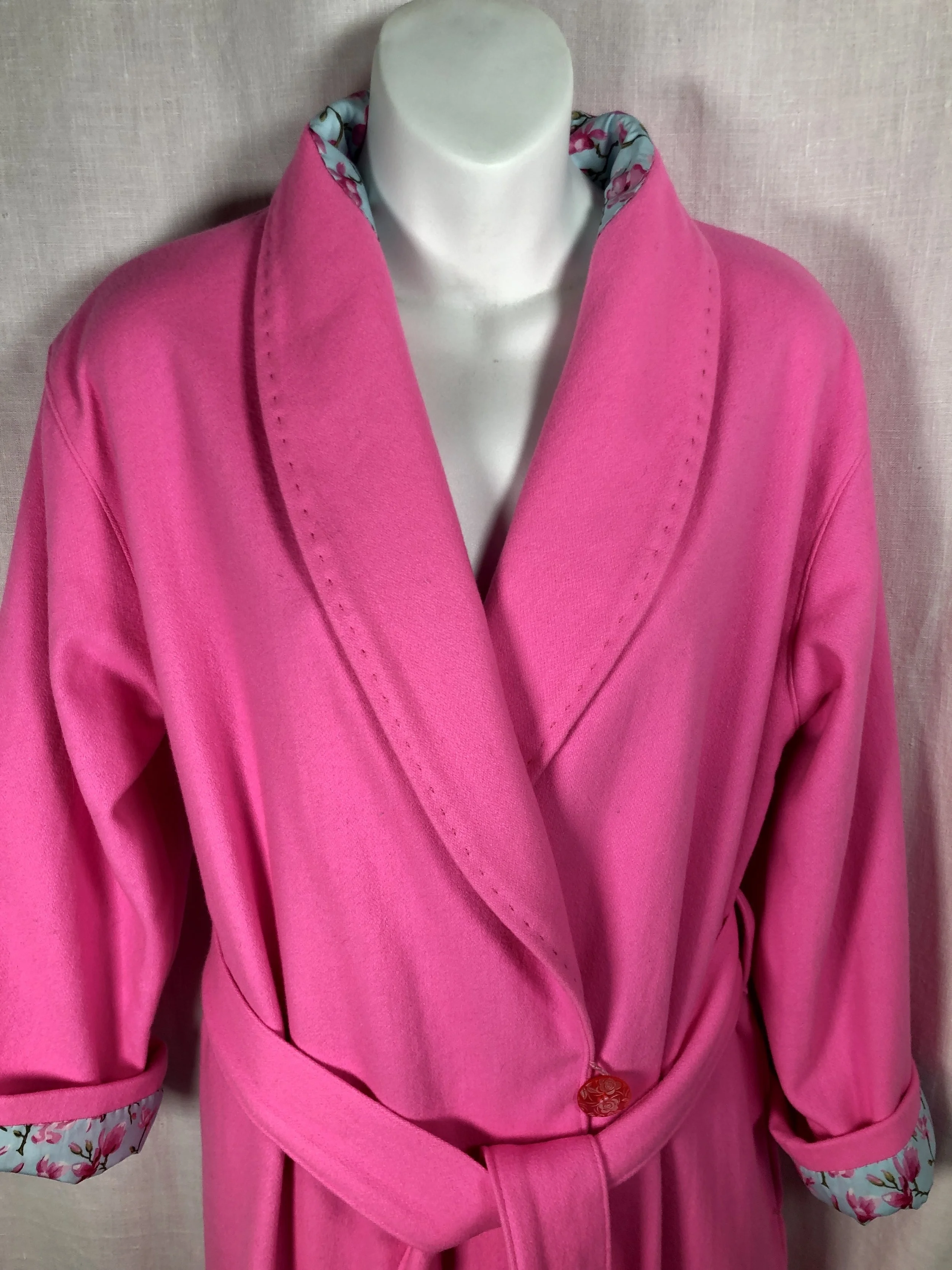 Pink bathrobe with floral cuffs and a waist belt displayed on a mannequin.