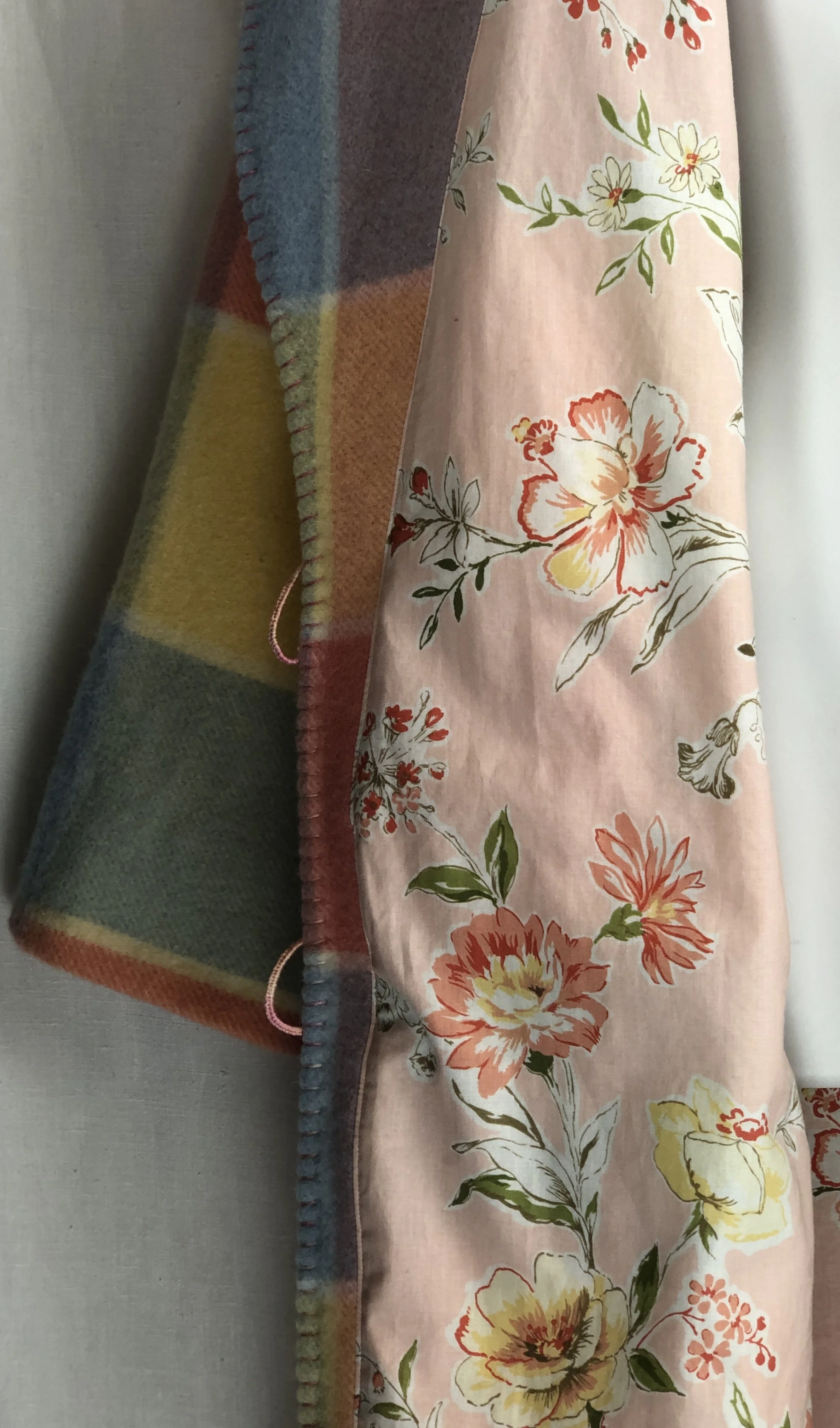 A colorful striped lining of a wool bathrobe and a pink floral fabric with large yellow and pink flowers on a light pink background hang side by side.