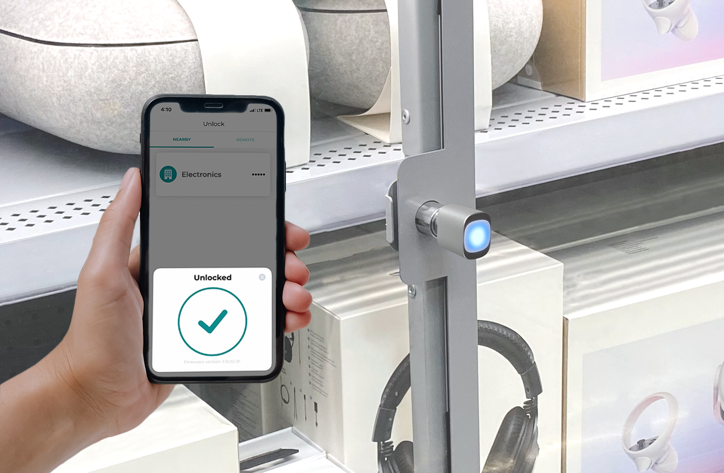 A person holding a smartphone displaying an unlocked message next to a smart lock in a retail setting, with electronics displayed on shelves.