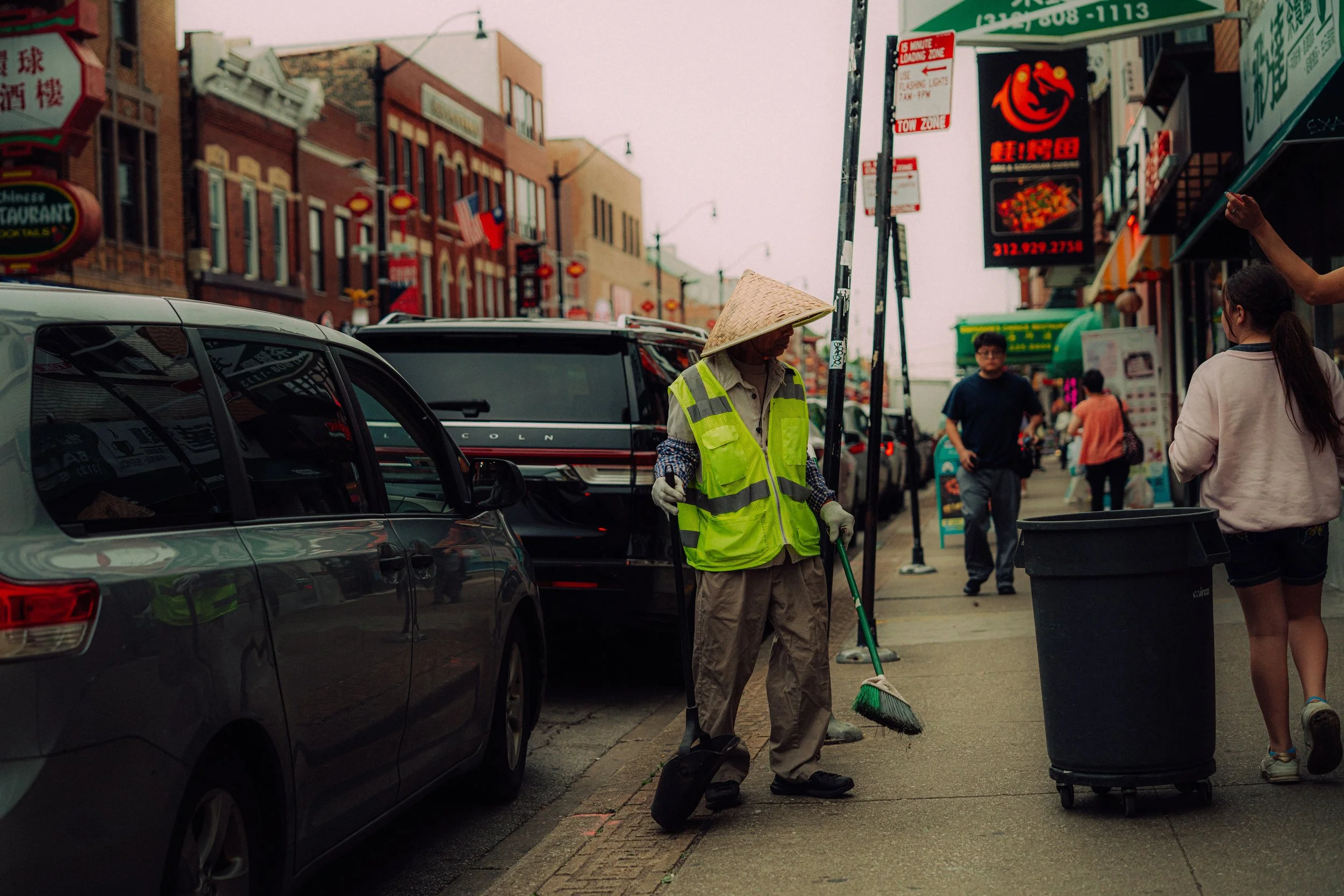 Wide street photograph of a worker wearing a reflective vest on a busy Chinatown, Chicago sidewalk.