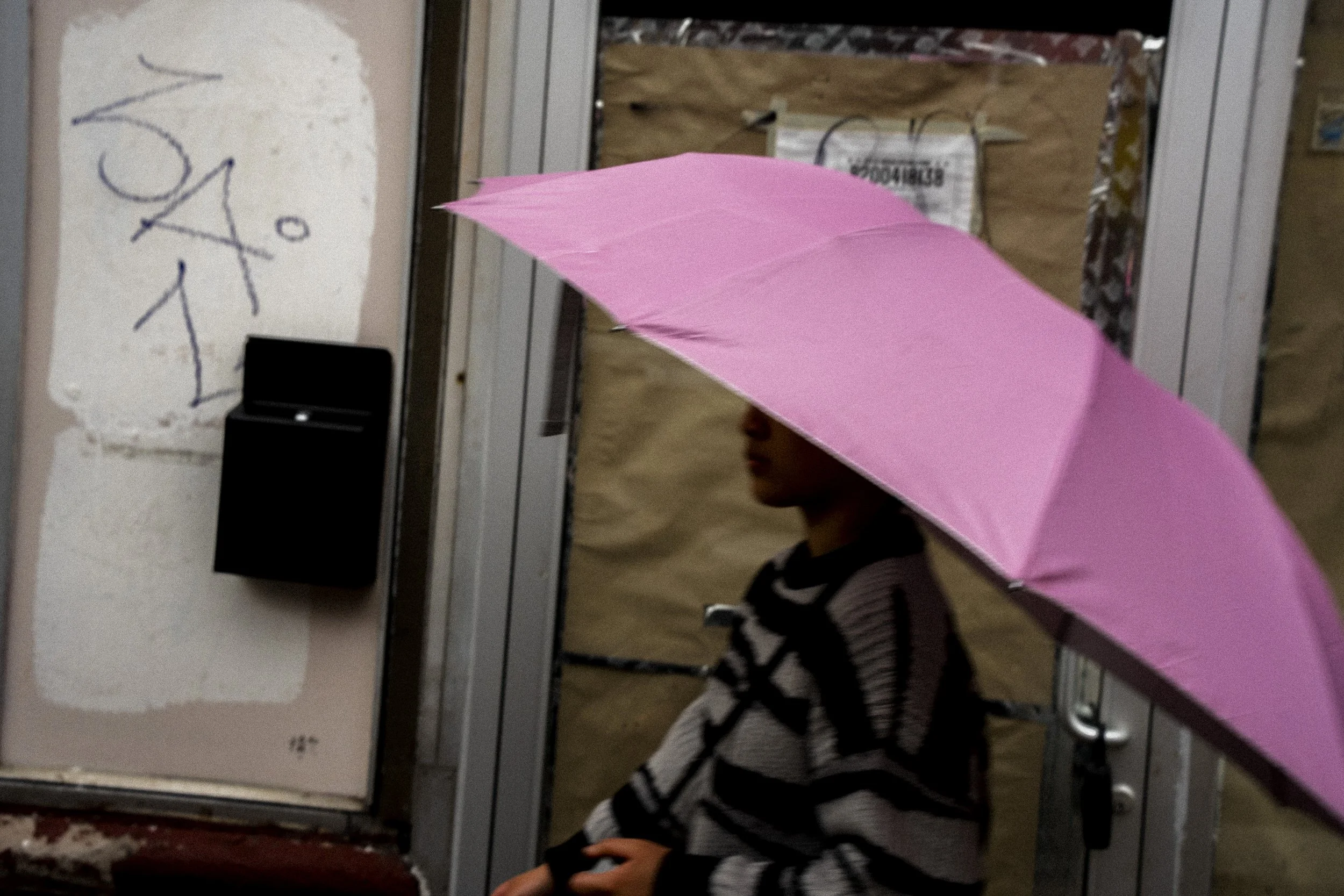 Close street photograph of a person beneath a pink umbrella passing a storefront in Chinatown, Chicago.