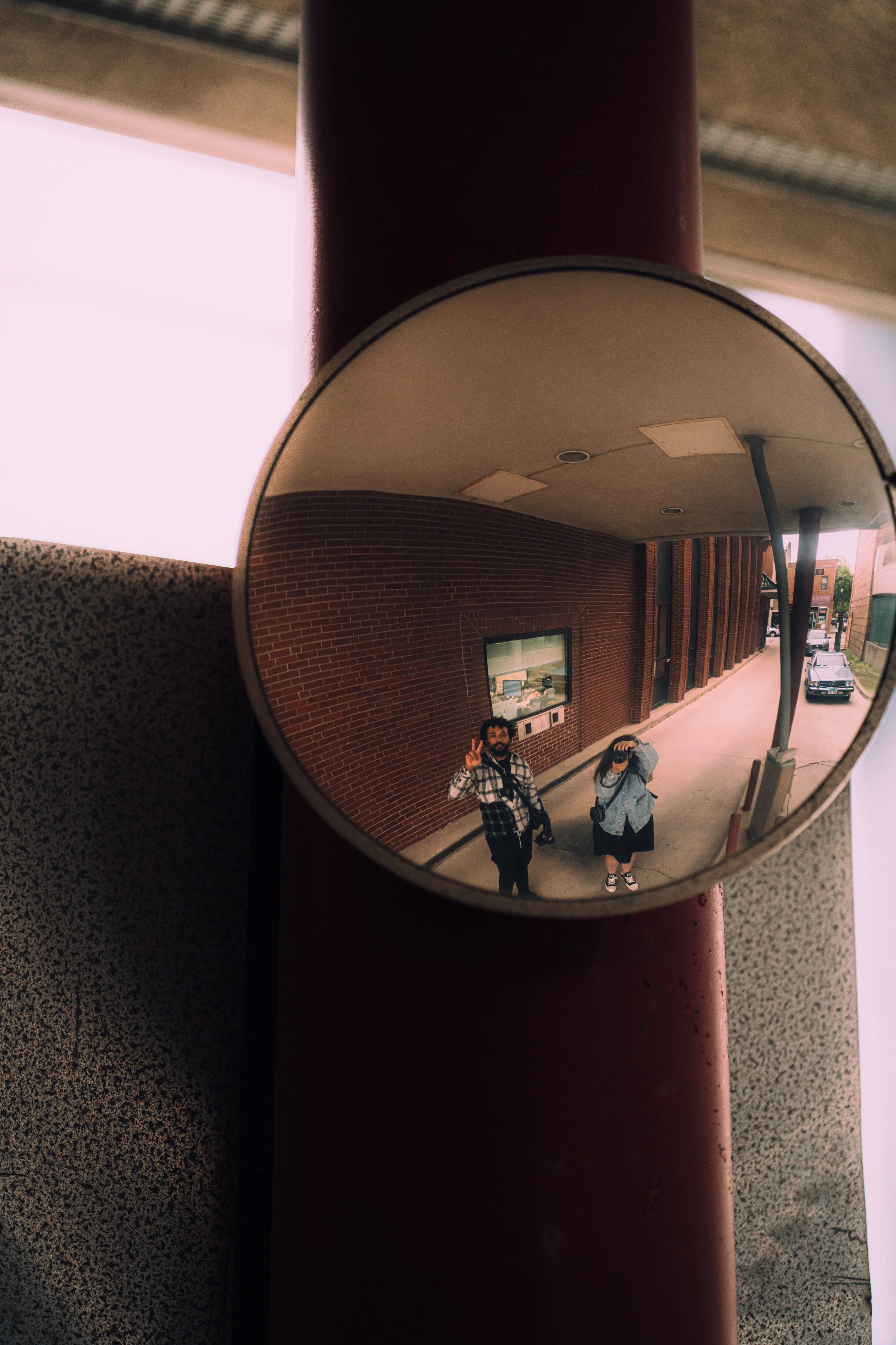 Two photographer — Rico J. Needham and Rahel reflected in a convex mirror while photographing each other on a Chinatown, Chicago street.