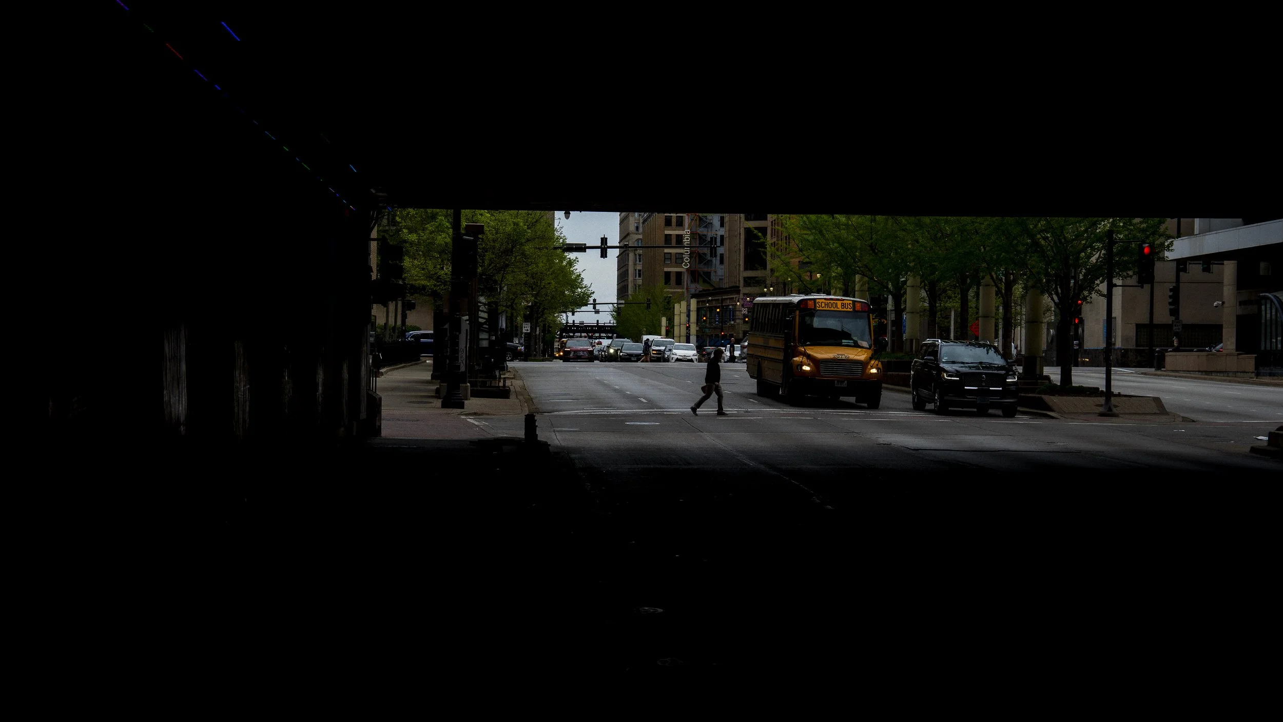 Pedestrian crossing a downtown Chicago street in front of a school bus, viewed from inside a dark tunnel.