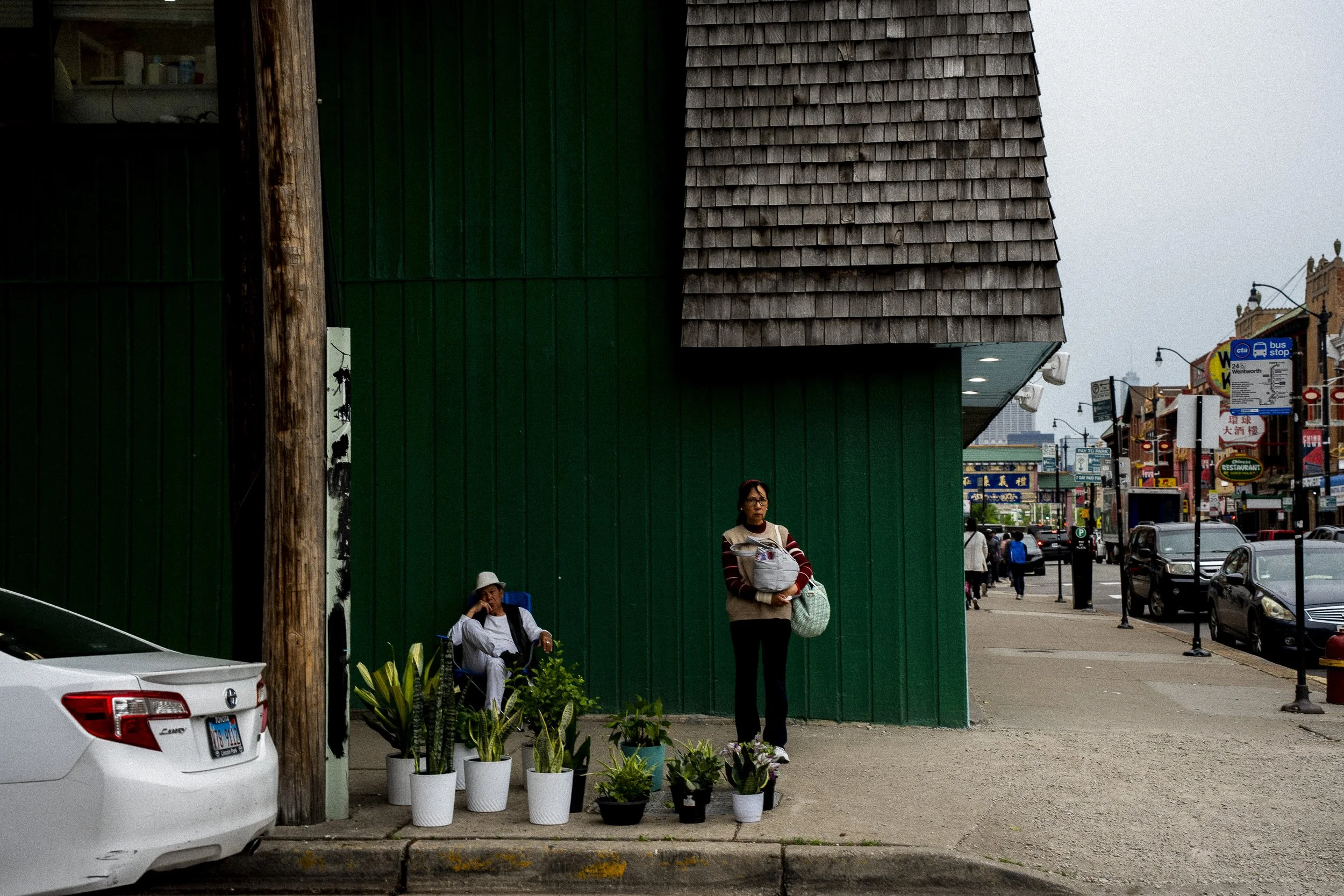 Wide street photograph of people outside a storefront with plants along a Chinatown, Chicago sidewalk.