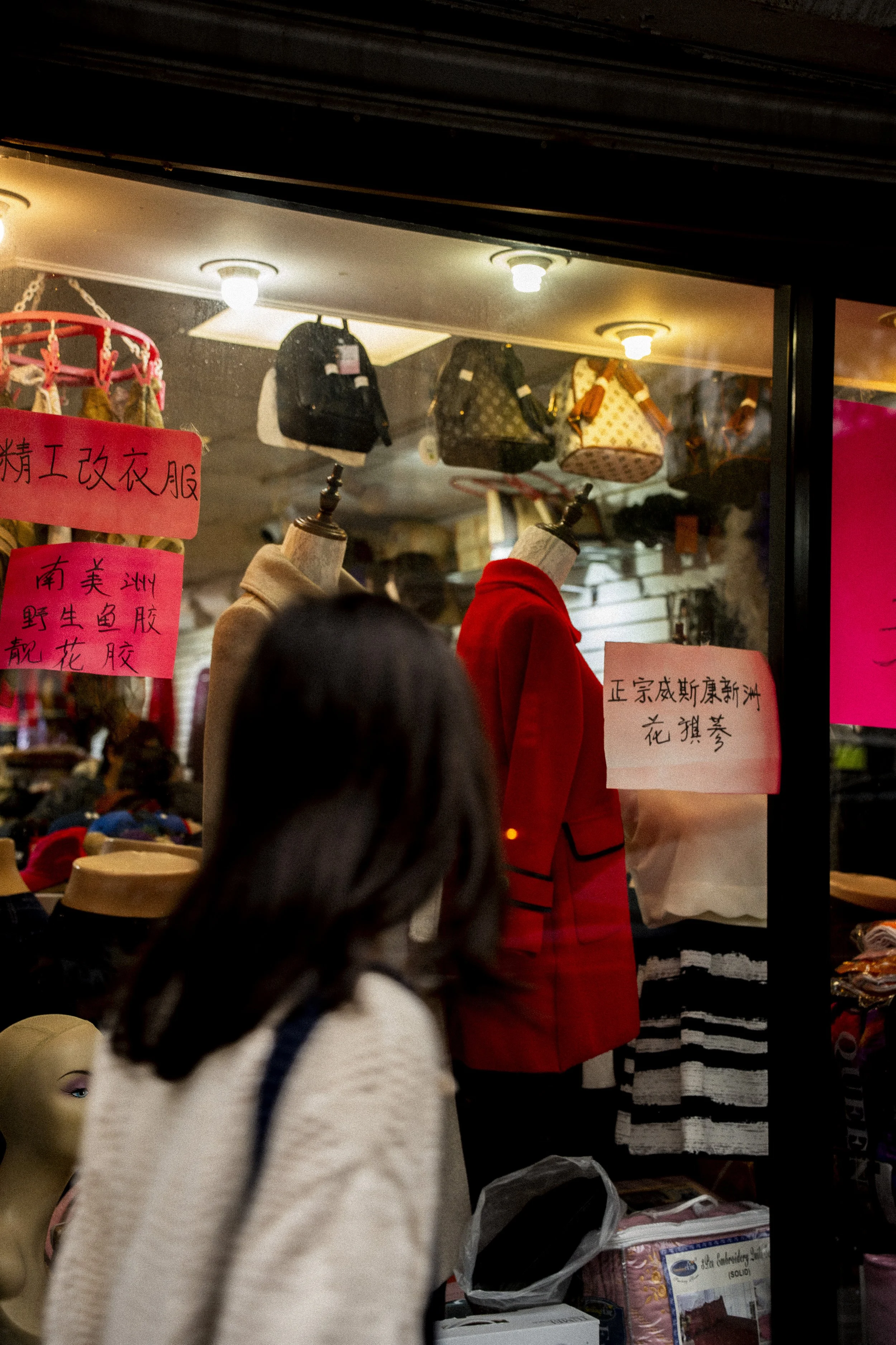 Street photograph of a blurred pedestrian passing mannequins and clothing in a Chinatown, Chicago storefront window.