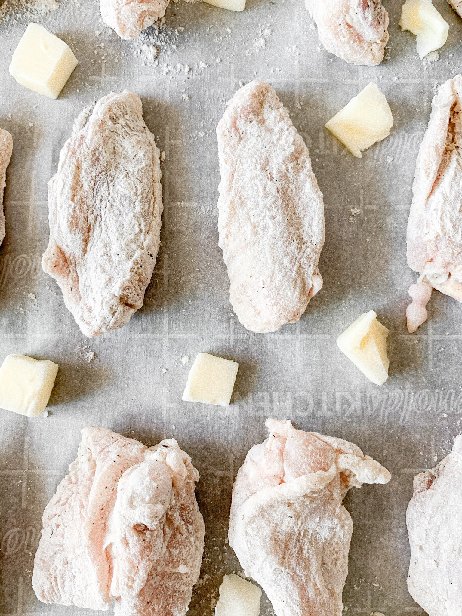 Chicken wings on a parchment lined baking sheet with knobs of butter